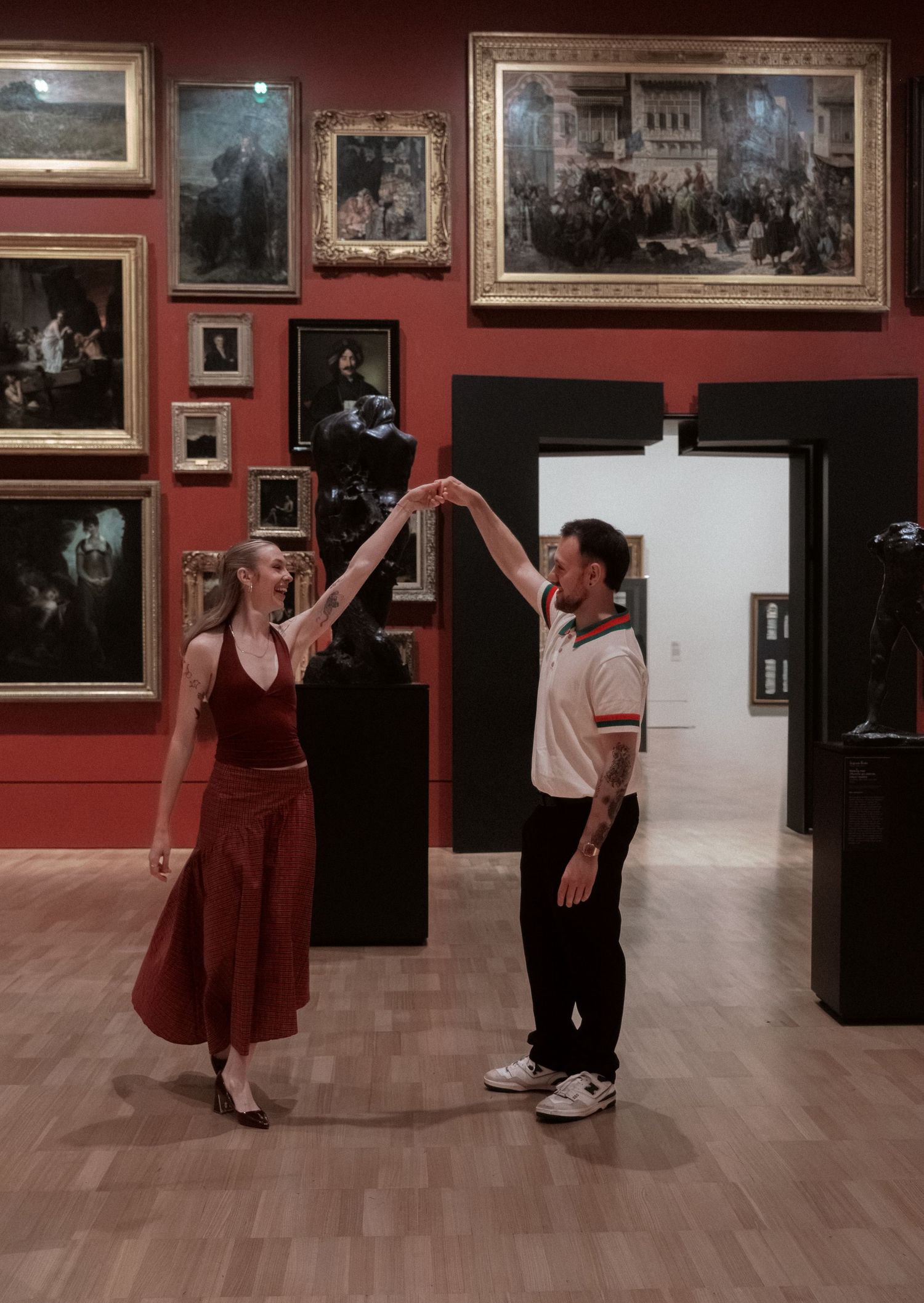 Couple dancing elegantly in a red-walled art museum gallery surrounded by classic paintings.