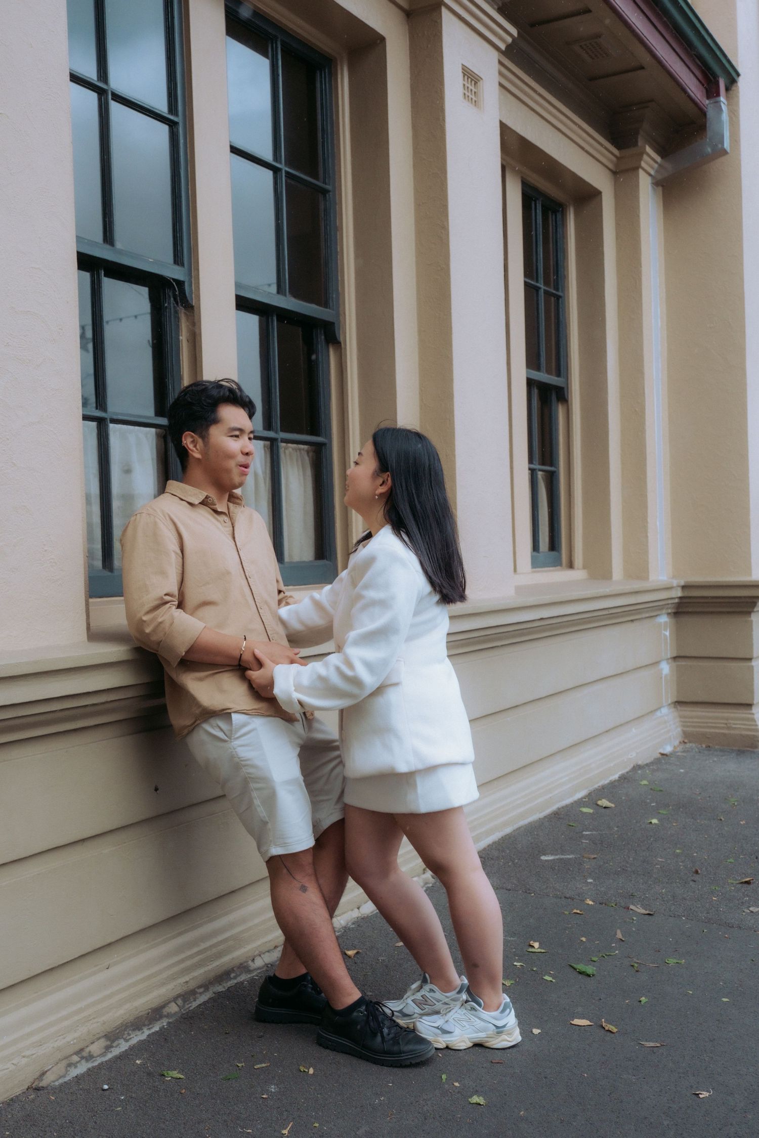 Couple holding hands and facing each other beside a cream-colored heritage building captured by Visuals By Dani Warrnambool photographer