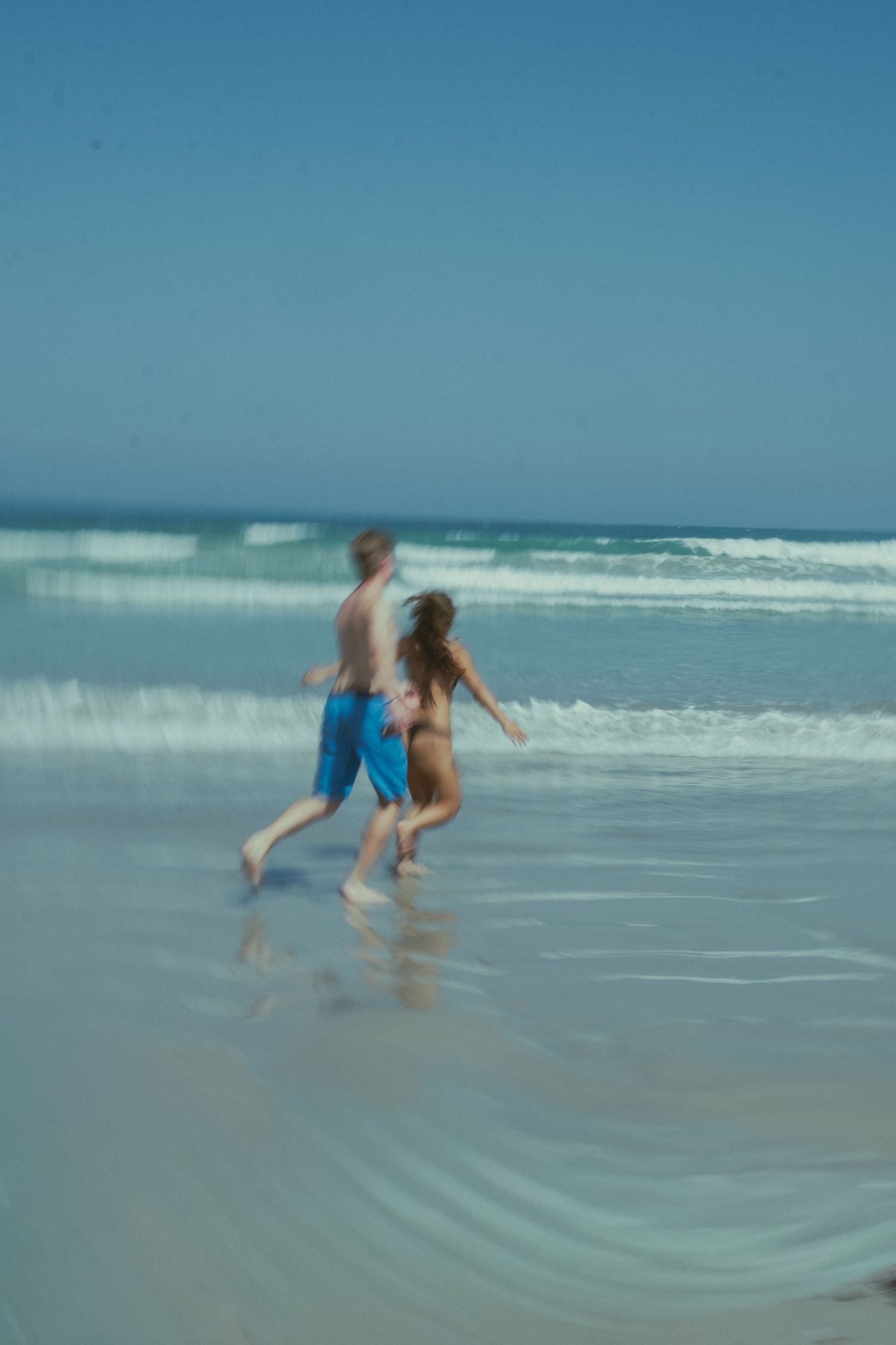 Blurry motion shot of a couple running along a sunny beach with ocean waves, Warrnambool beach.