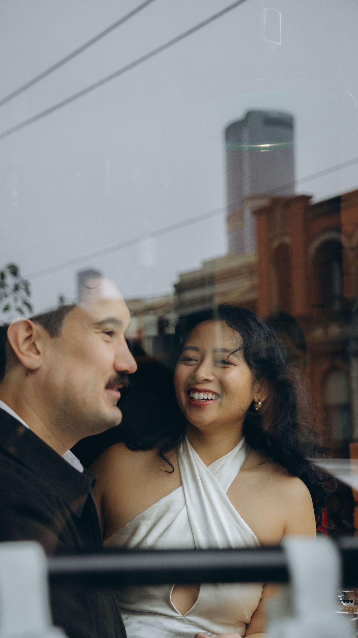 A joyful couple shares a romantic moment, smiling together near a window with a city backdrop.