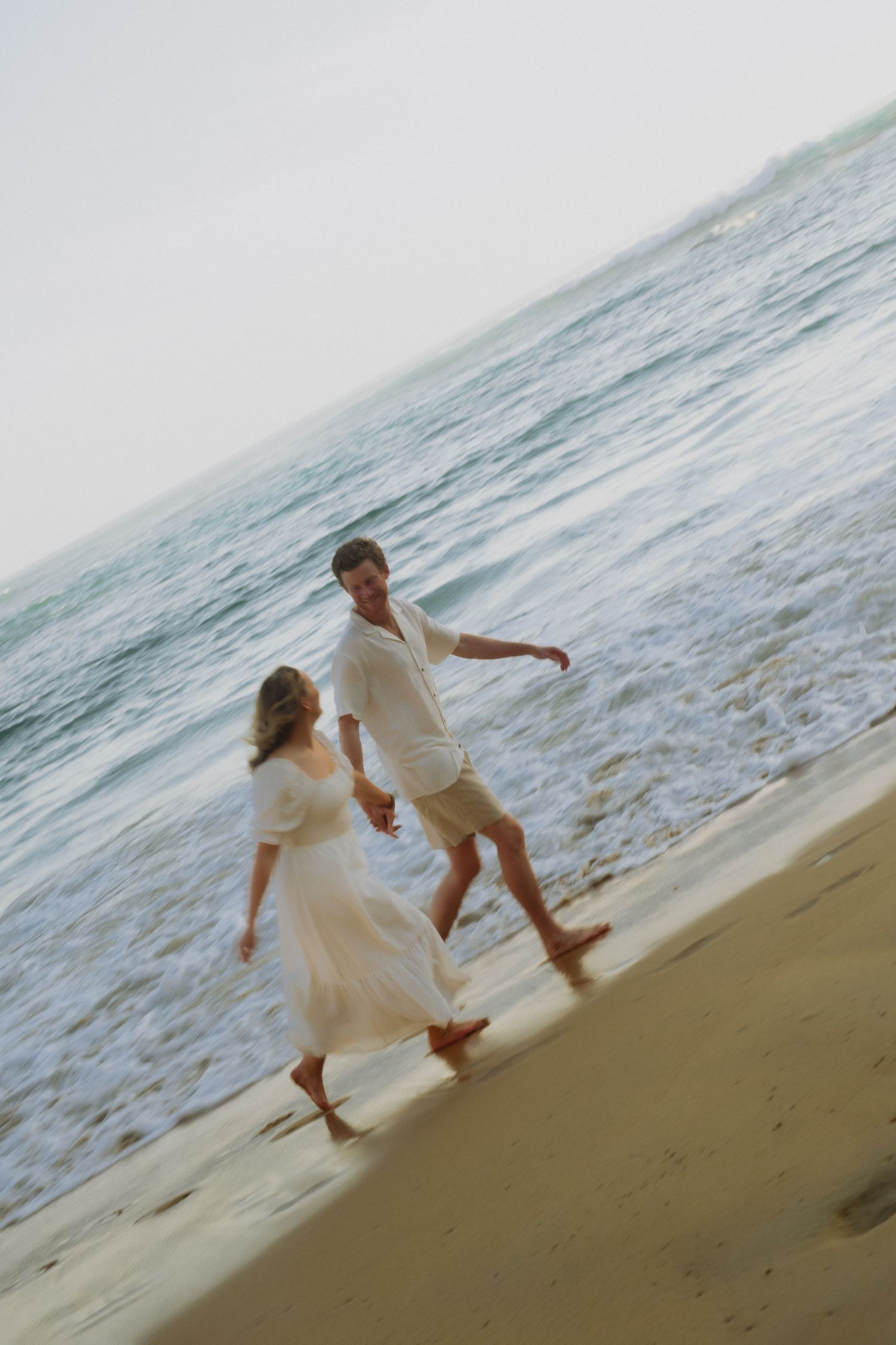 Warrnambool couples photographer captures happy couple holding hands and walking barefoot along a sandy beach at dusk.