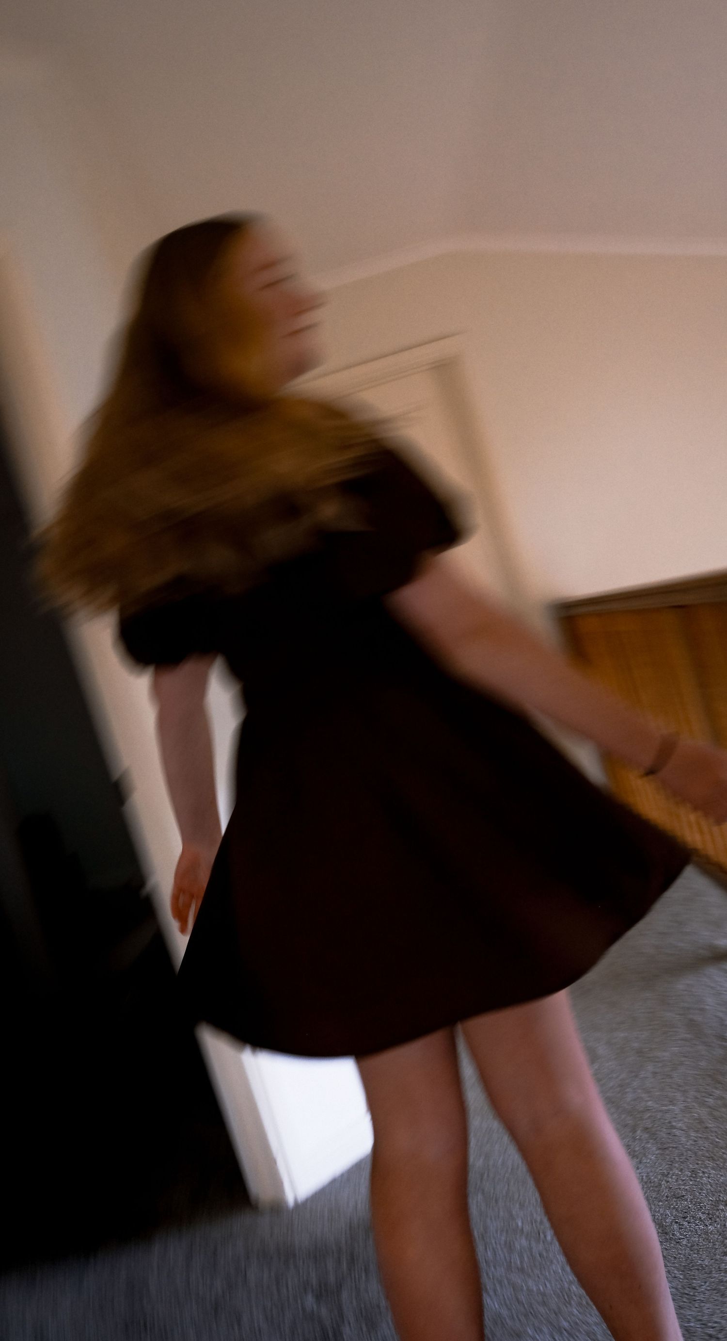 Blurred motion shot of a young woman in a black off-shoulder dress spinning indoors.