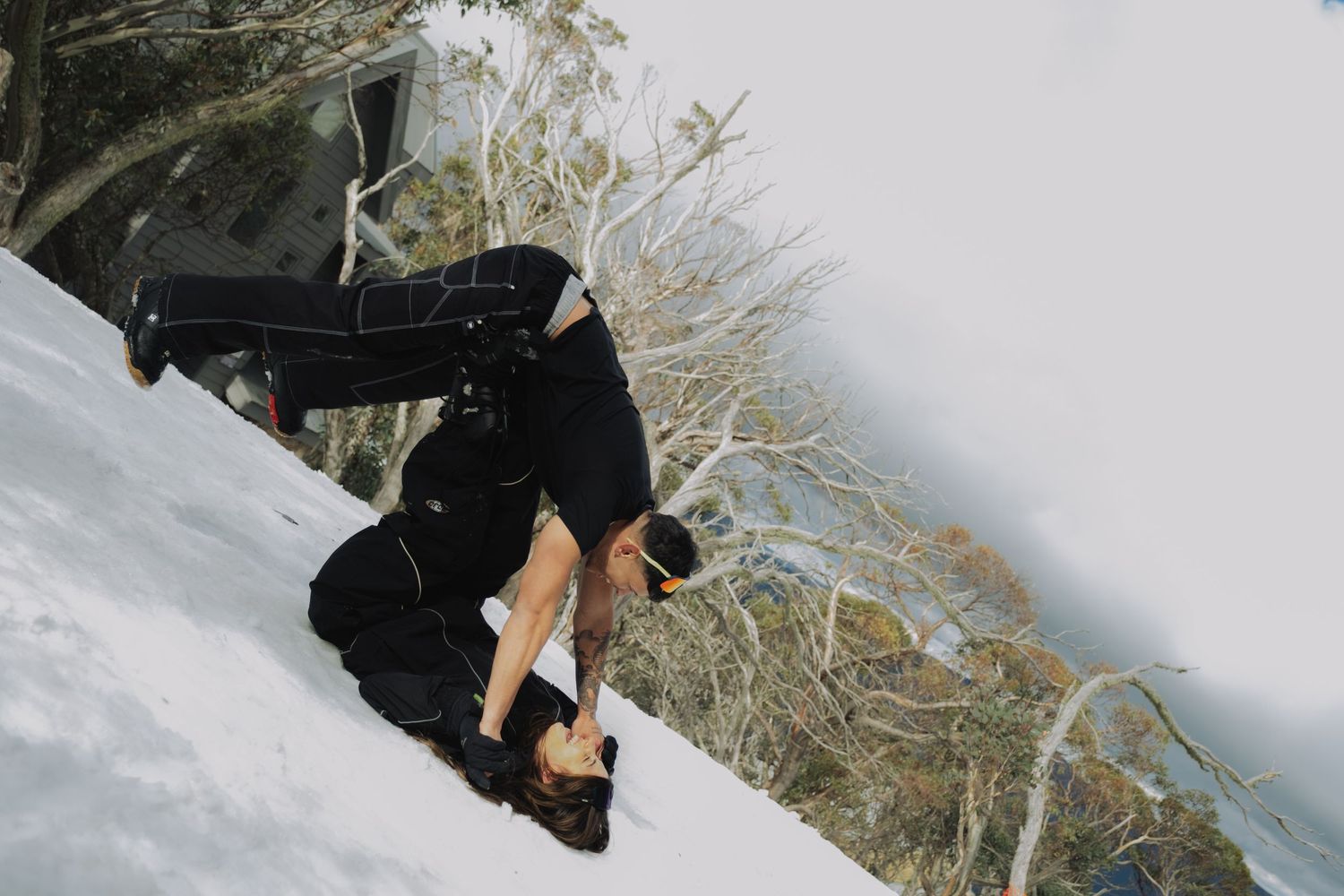 Person tumbling down a snowy slope in black clothing surrounded by snow-covered trees.