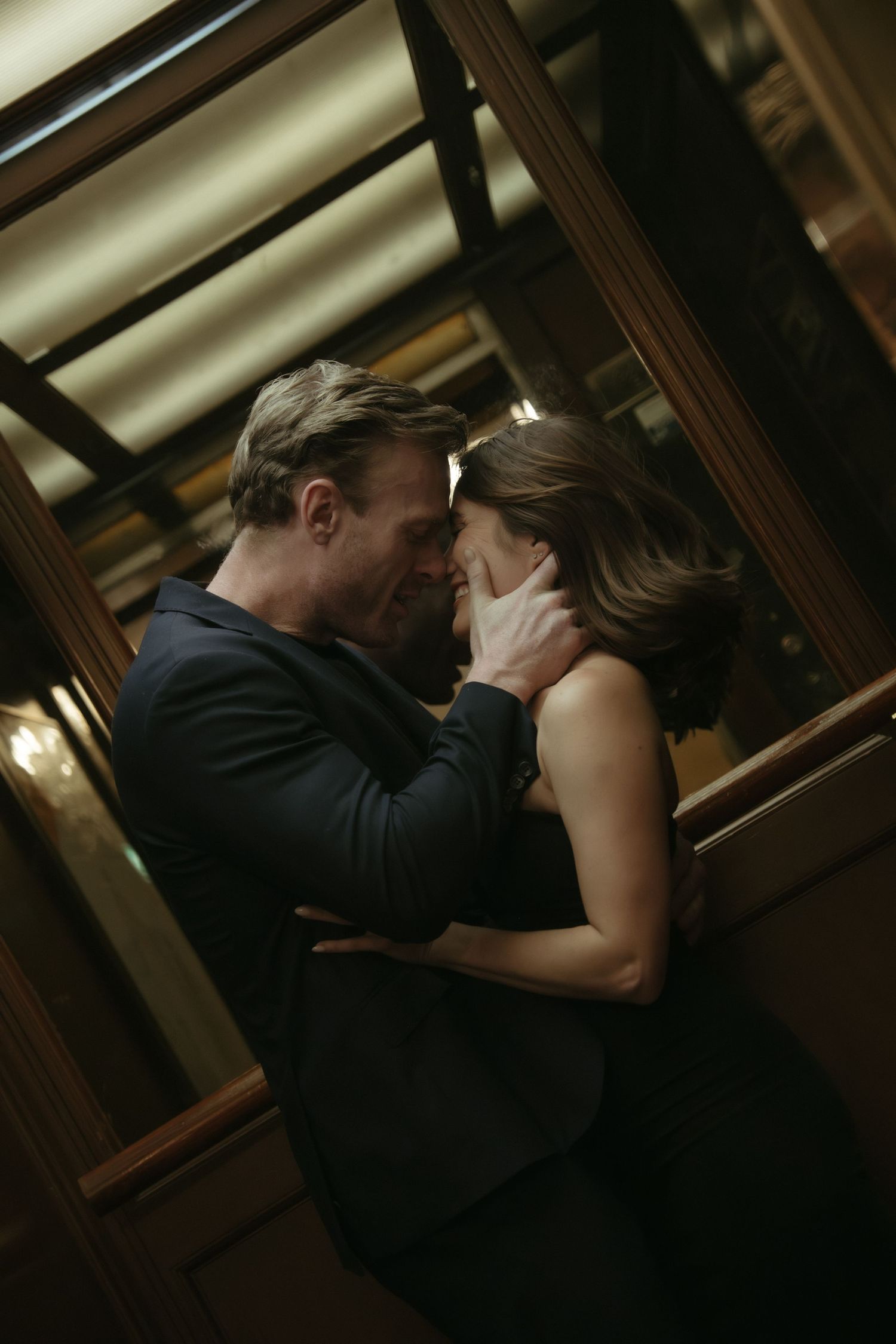 A couple sharing an intimate moment, man tenderly holding woman's face in a dimly lit elegant interior.