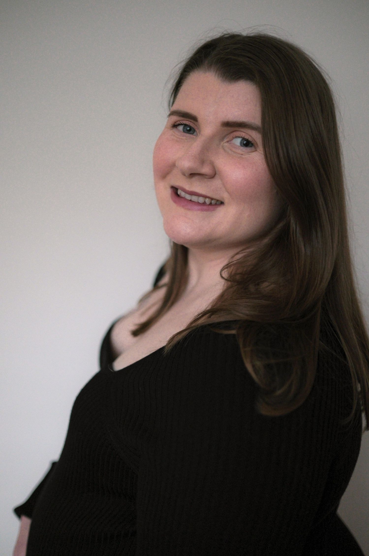 Smiling pregnant woman with brown hair wearing black top against white background.