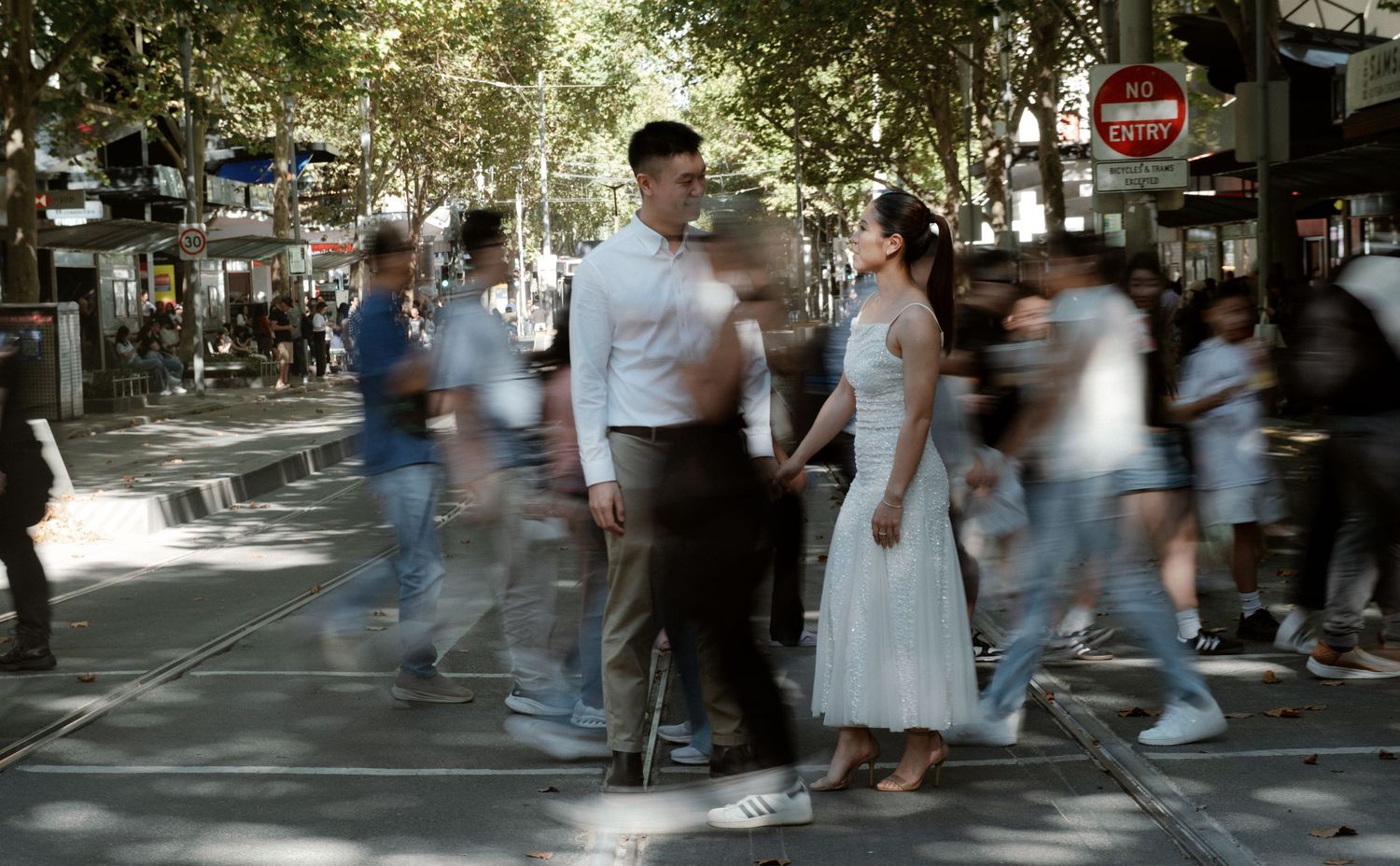Couple stands still amid blurred crowd on busy urban street, long exposure photography capturing motion blur.