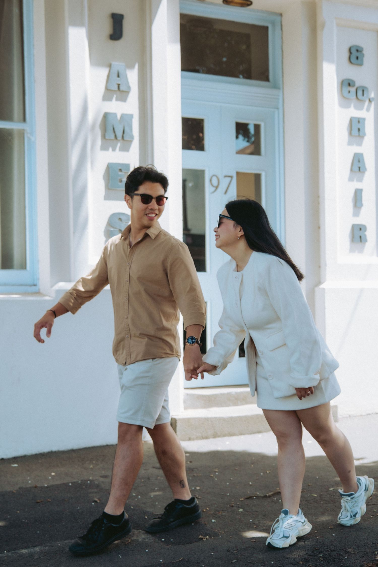 Smiling couple holding hands and walking past a Warrnambool storefront - captured by Visuals By Dani Warrnambool photographer