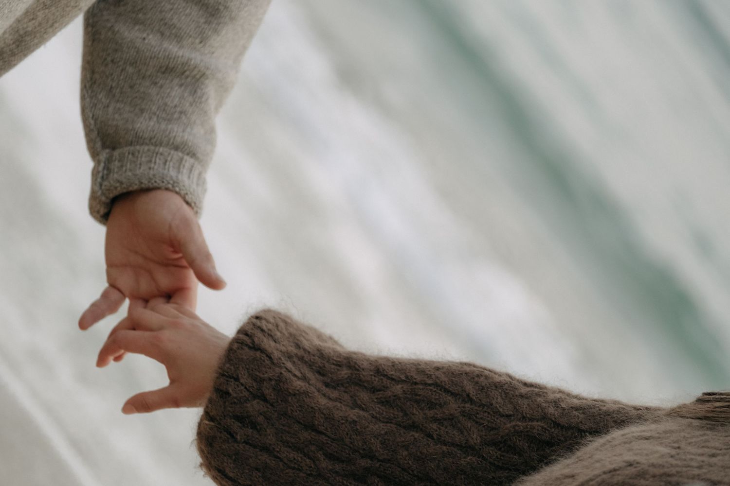 Close-up of two people gently touching hands while wearing cozy knit sweaters outdoors.