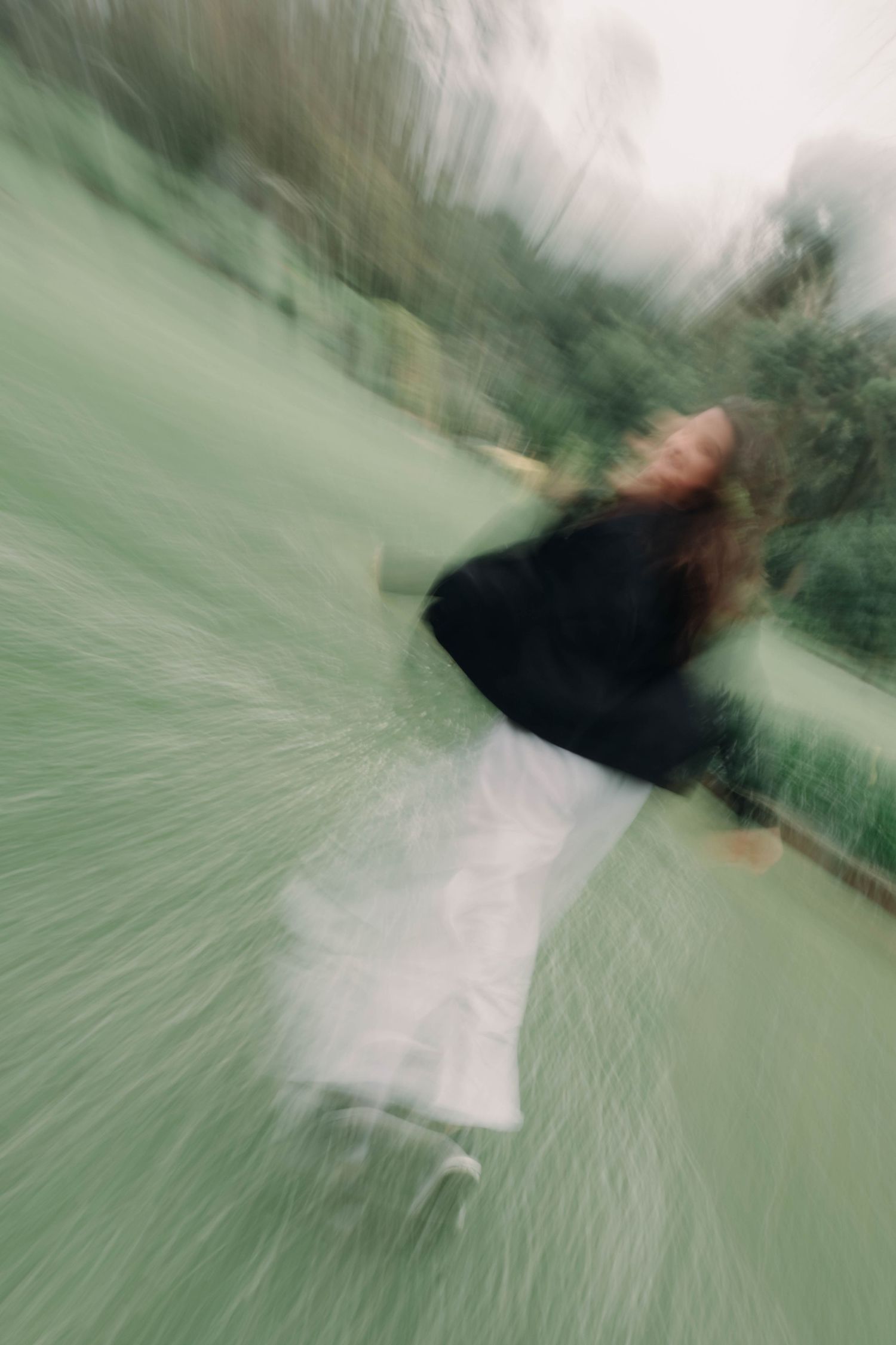 Artistic motion blur photograph of a woman in black and white outfit spinning outdoors in a park.