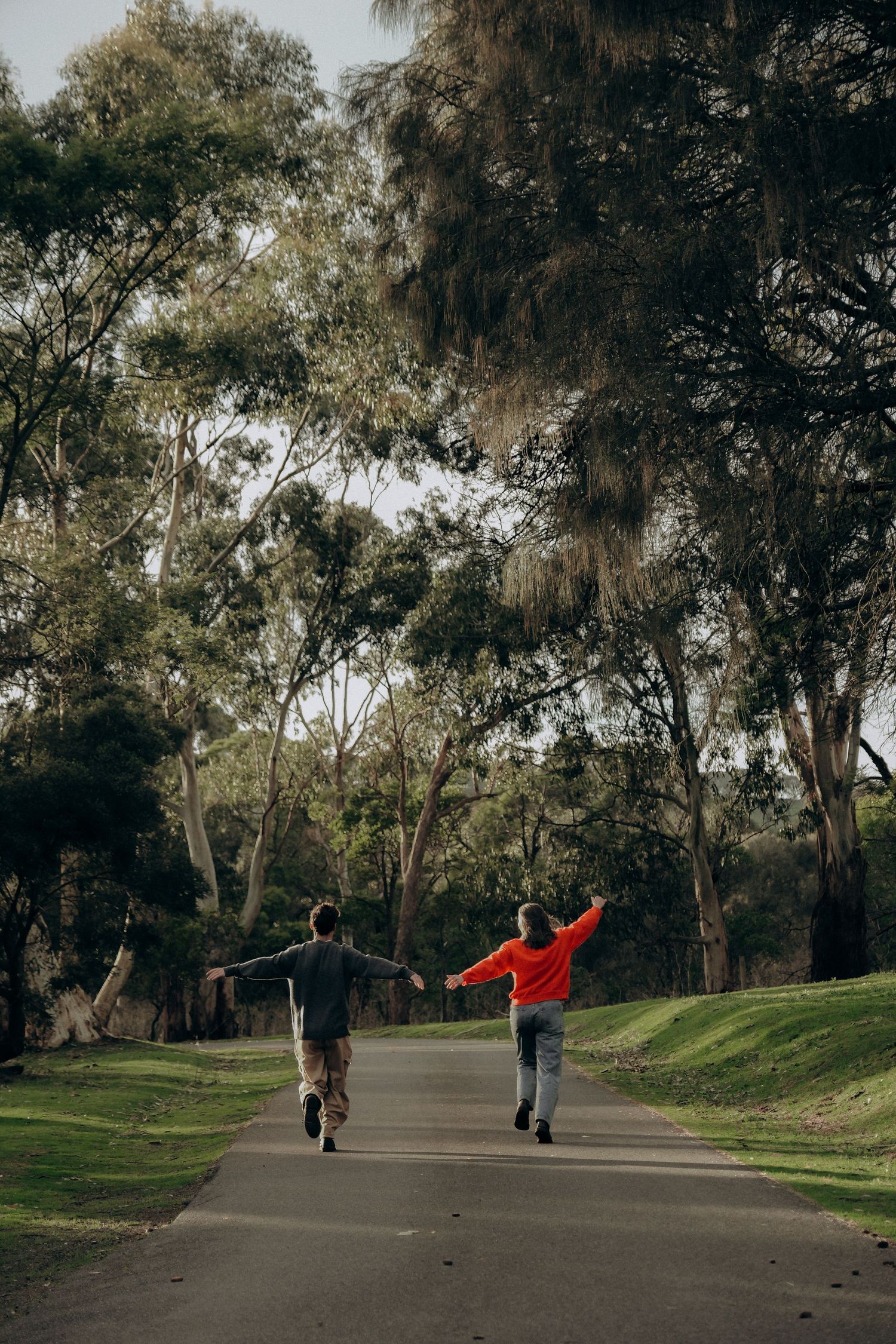 Two children running joyfully down a tree-lined path in a lush green park on an overcast day.