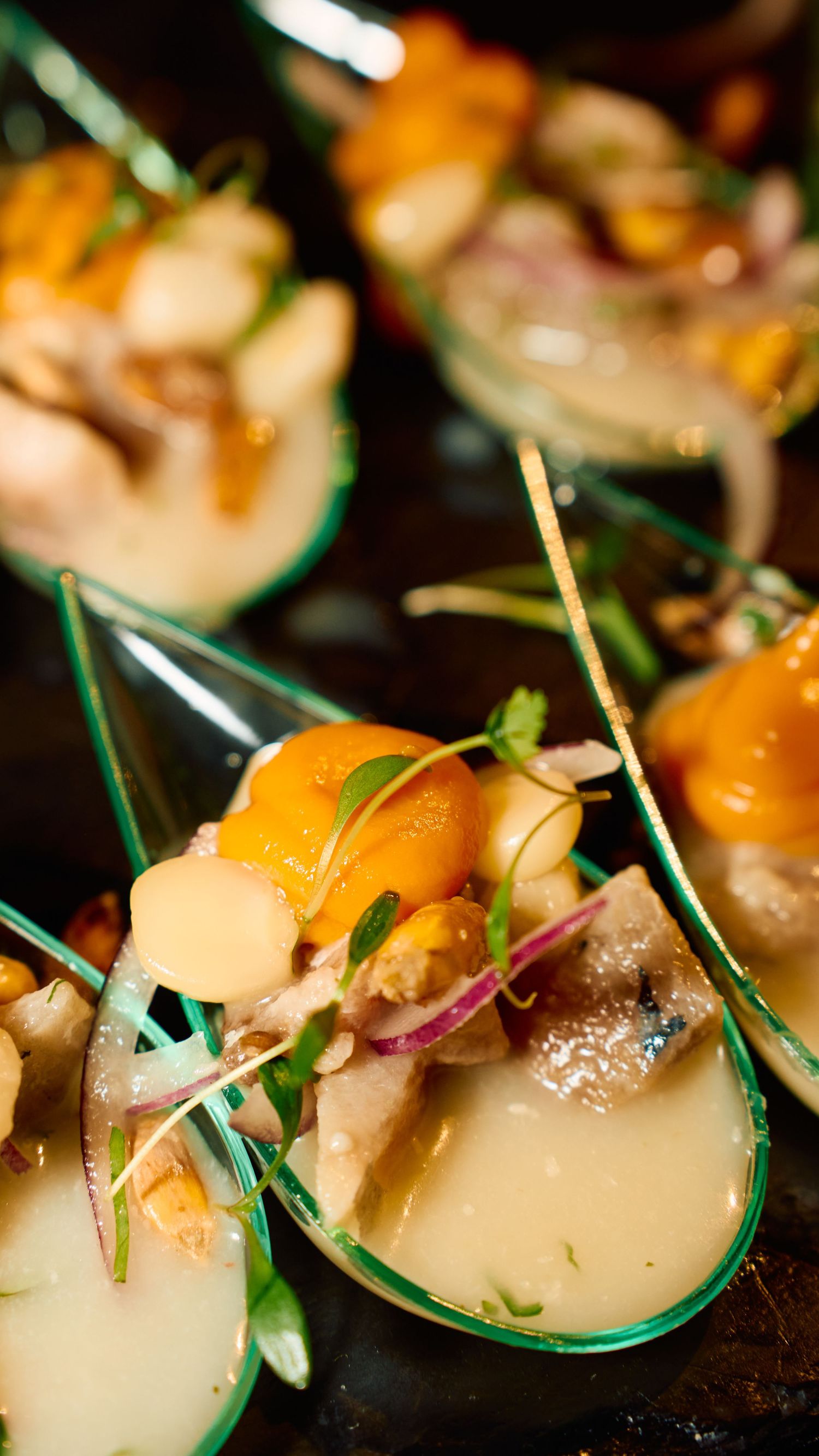 Elegant appetizers served in green spoons with citrus and microgreens garnish.