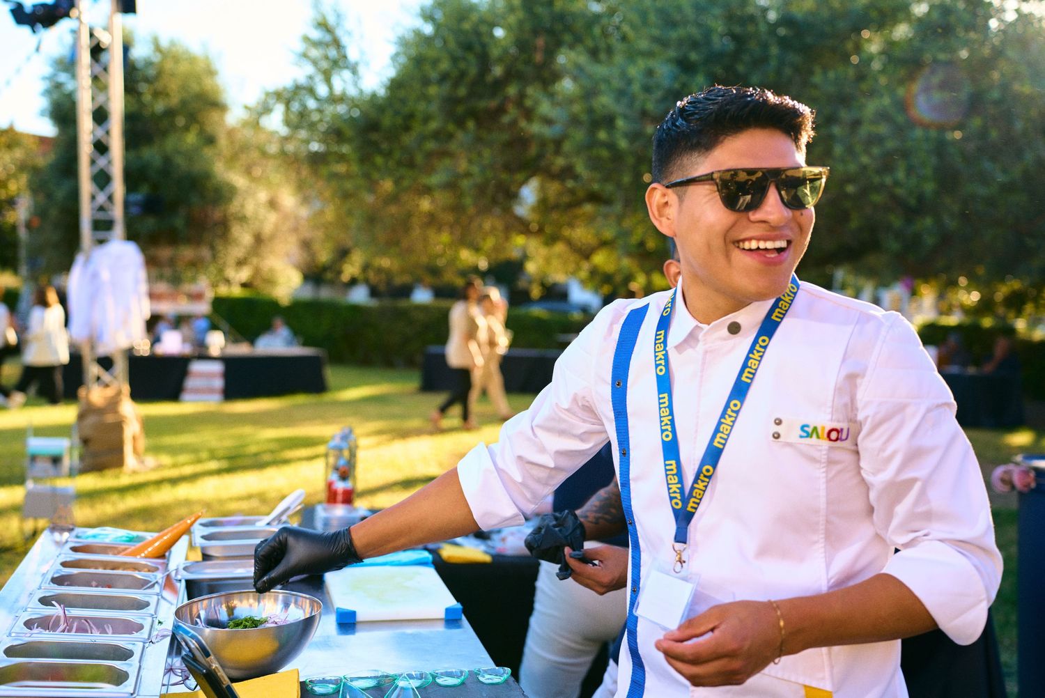 Chef preparing food at an outdoor catering station during a sunny event.