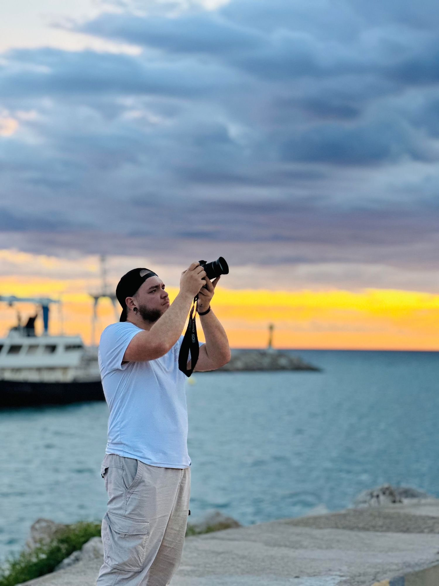 Photographer capturing sunset photos at a waterfront location with dramatic cloudy sky.