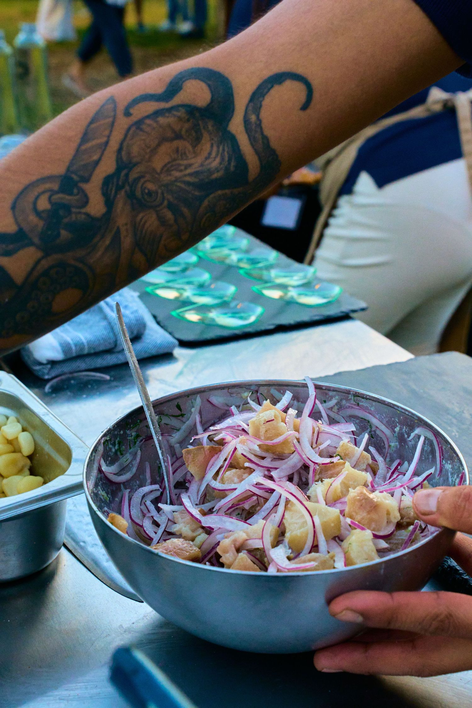 A bowl of fresh ceviche being prepared with red onions and visible octopus tattoo in background.