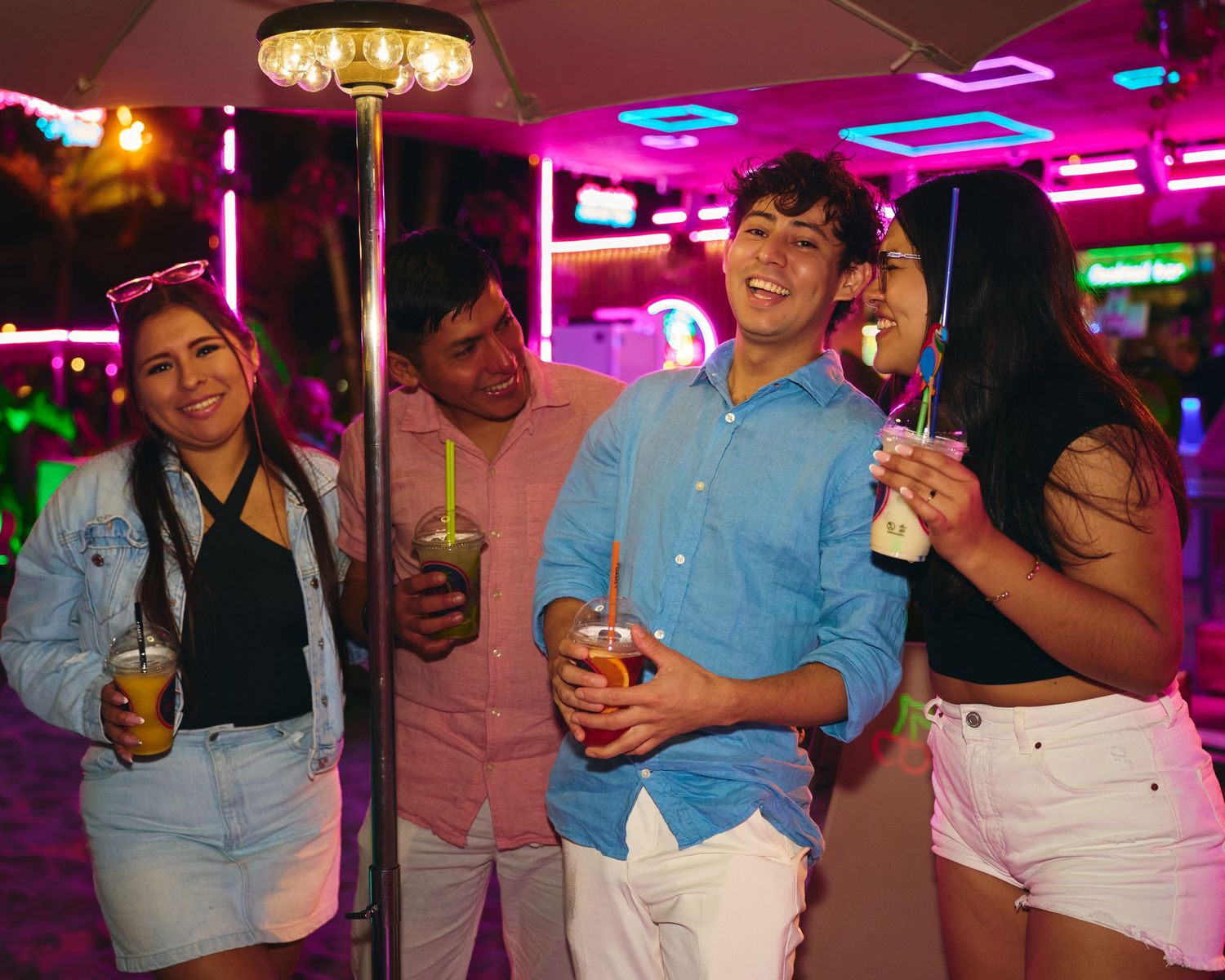 Group posing with beverages under pink neon lights at a nightclub.