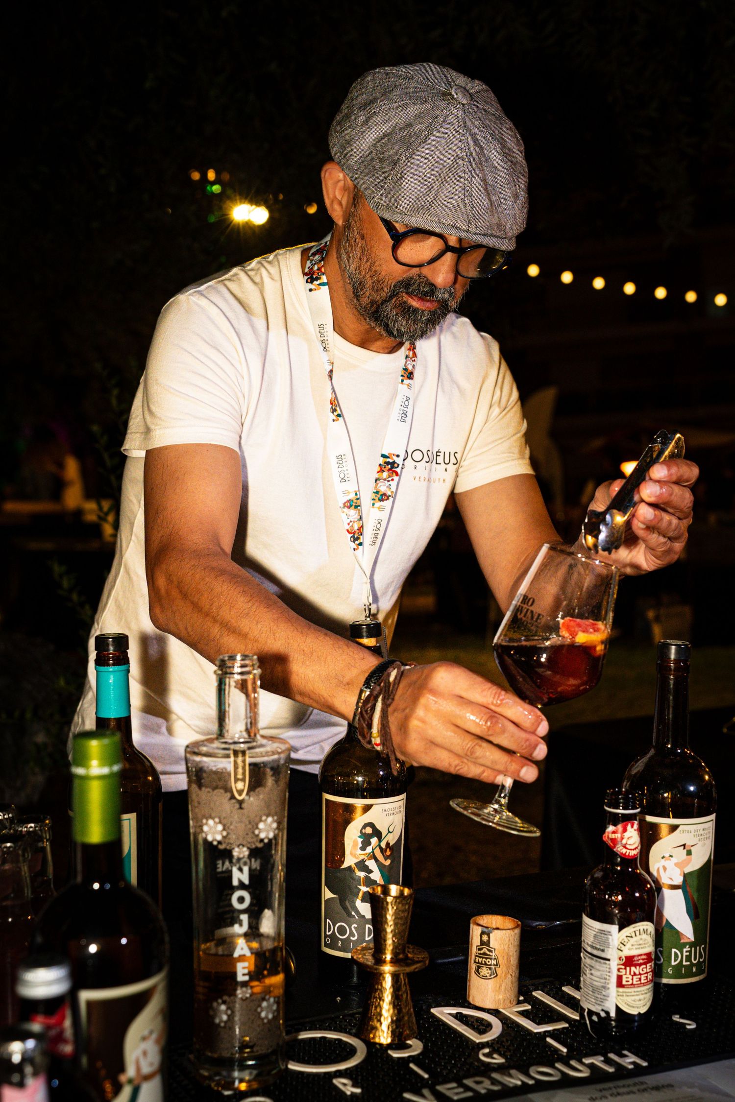 Bartender preparing craft cocktails at a dimly lit bar with various spirits and ingredients.