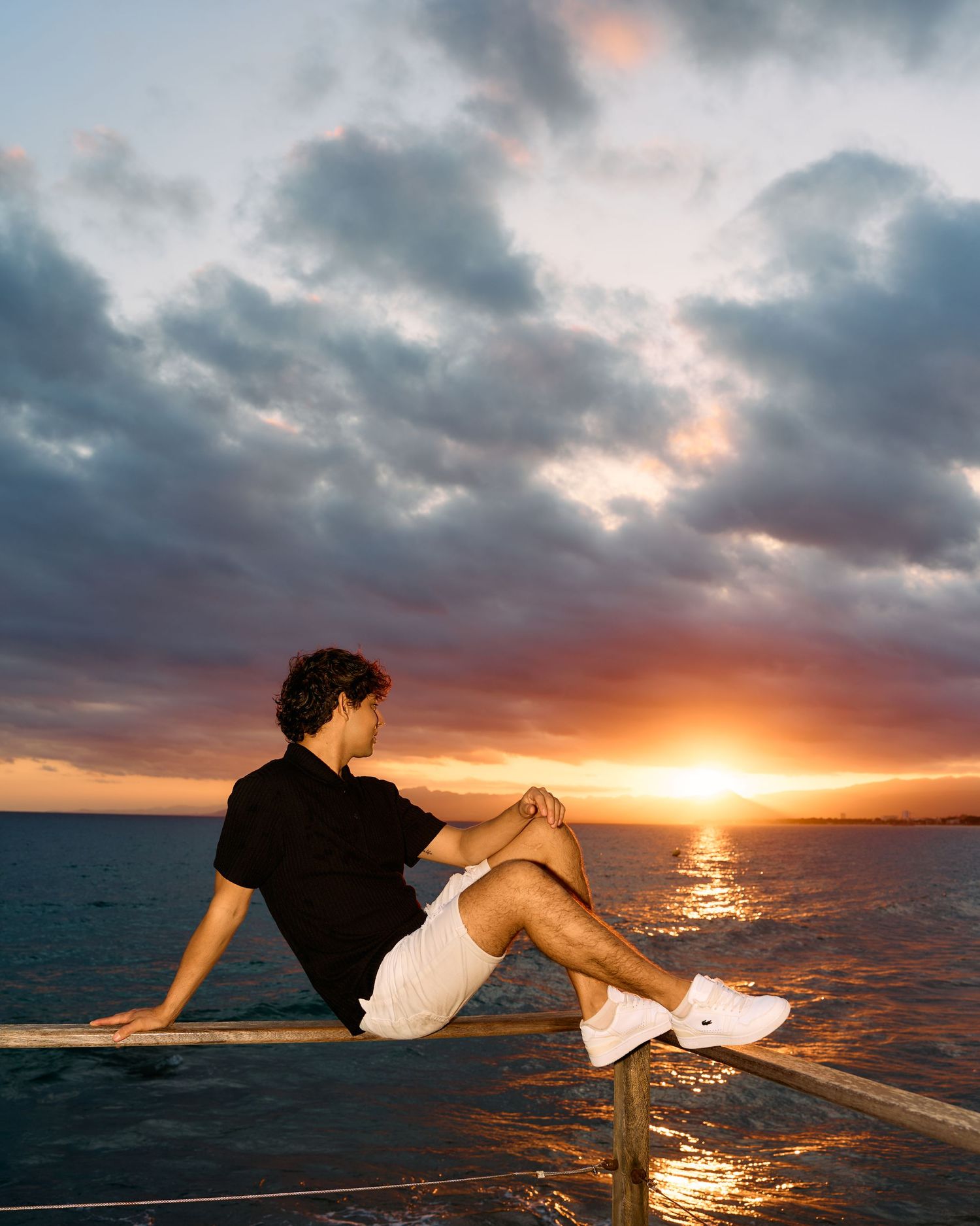 Silhouette relaxing on railing against dramatic sunset over ocean horizon.