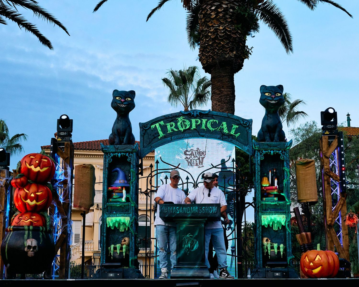Halloween decorations with black cat statues and a 'Tropical' sign arch at an amusement park entrance.