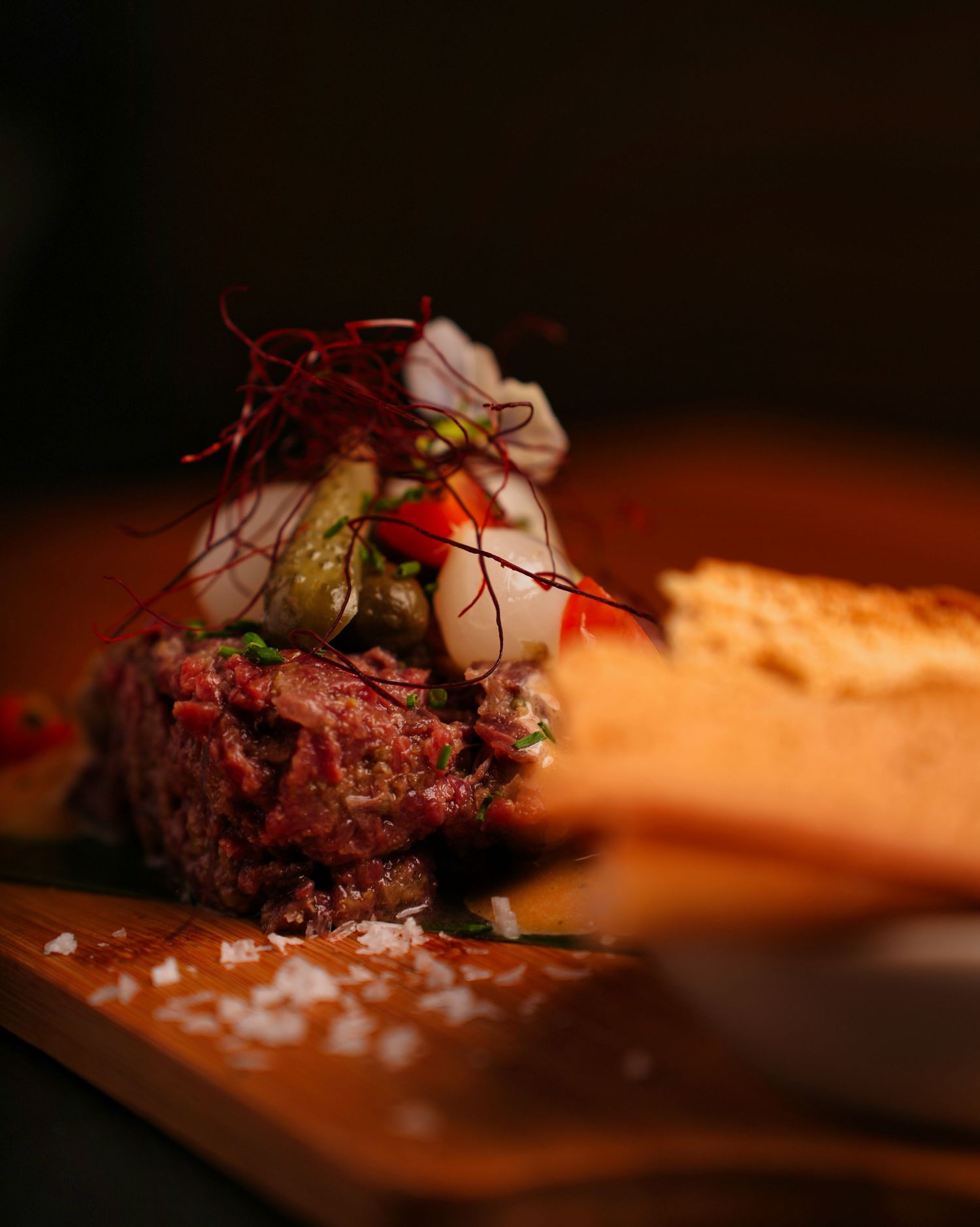 Close-up of grilled meat with herbs and seasoning on a wooden surface in dramatic lighting.