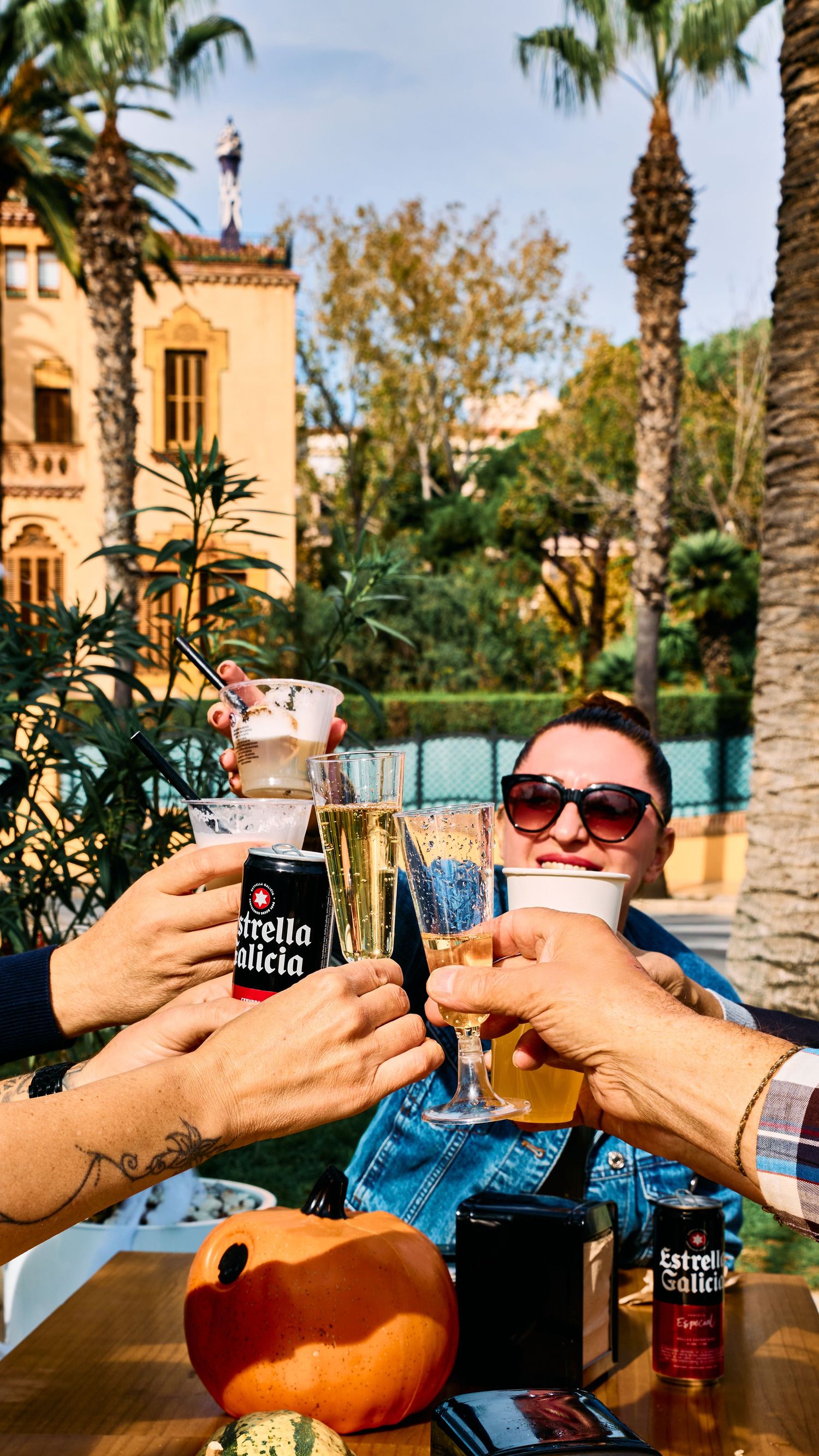 Friends toasting drinks at an outdoor restaurant with palm trees and Spanish architecture.