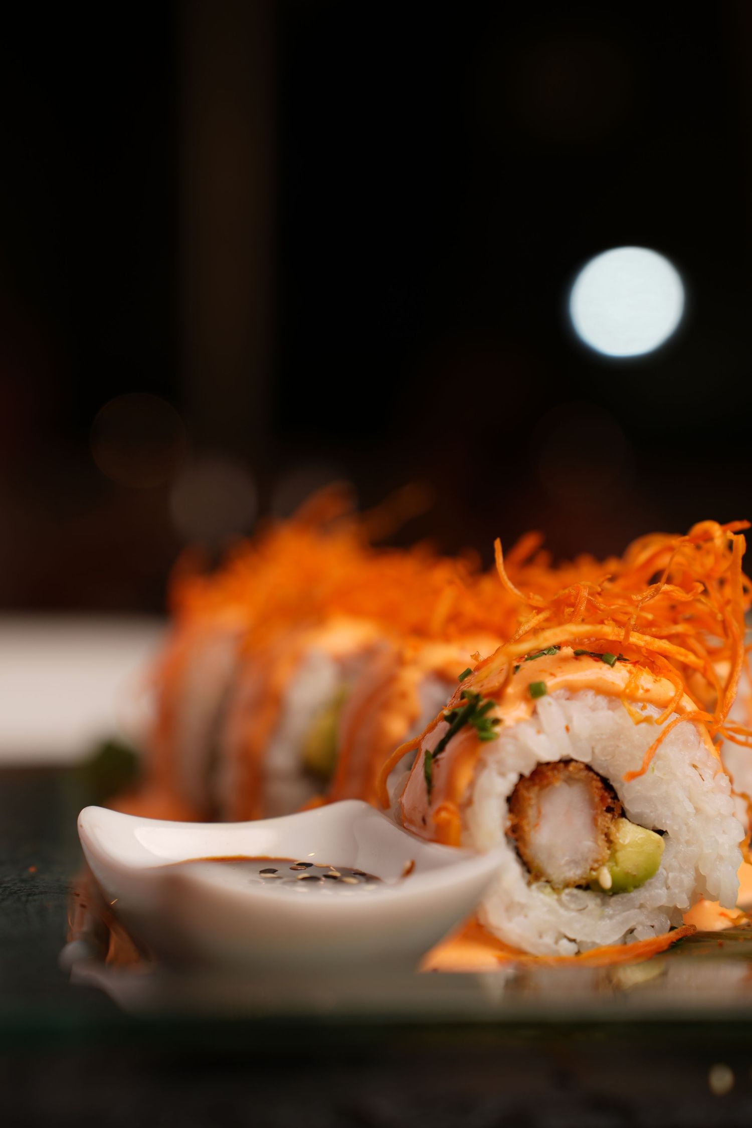 Close-up of crispy orange-topped sushi roll with dipping sauce.