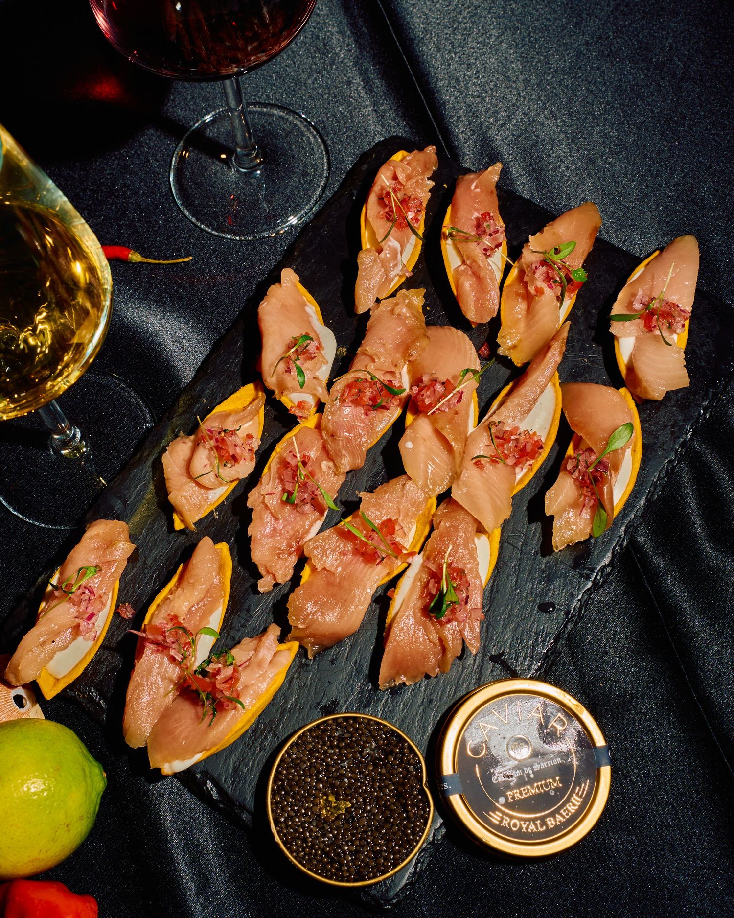 Elegant appetizers with caviar and wine glasses arranged on a dark slate platter.