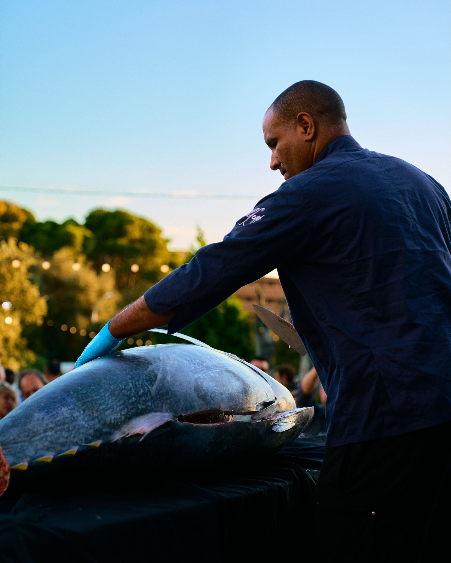 Chef preparing fresh fish during golden hour sunset at an outdoor kitchen.