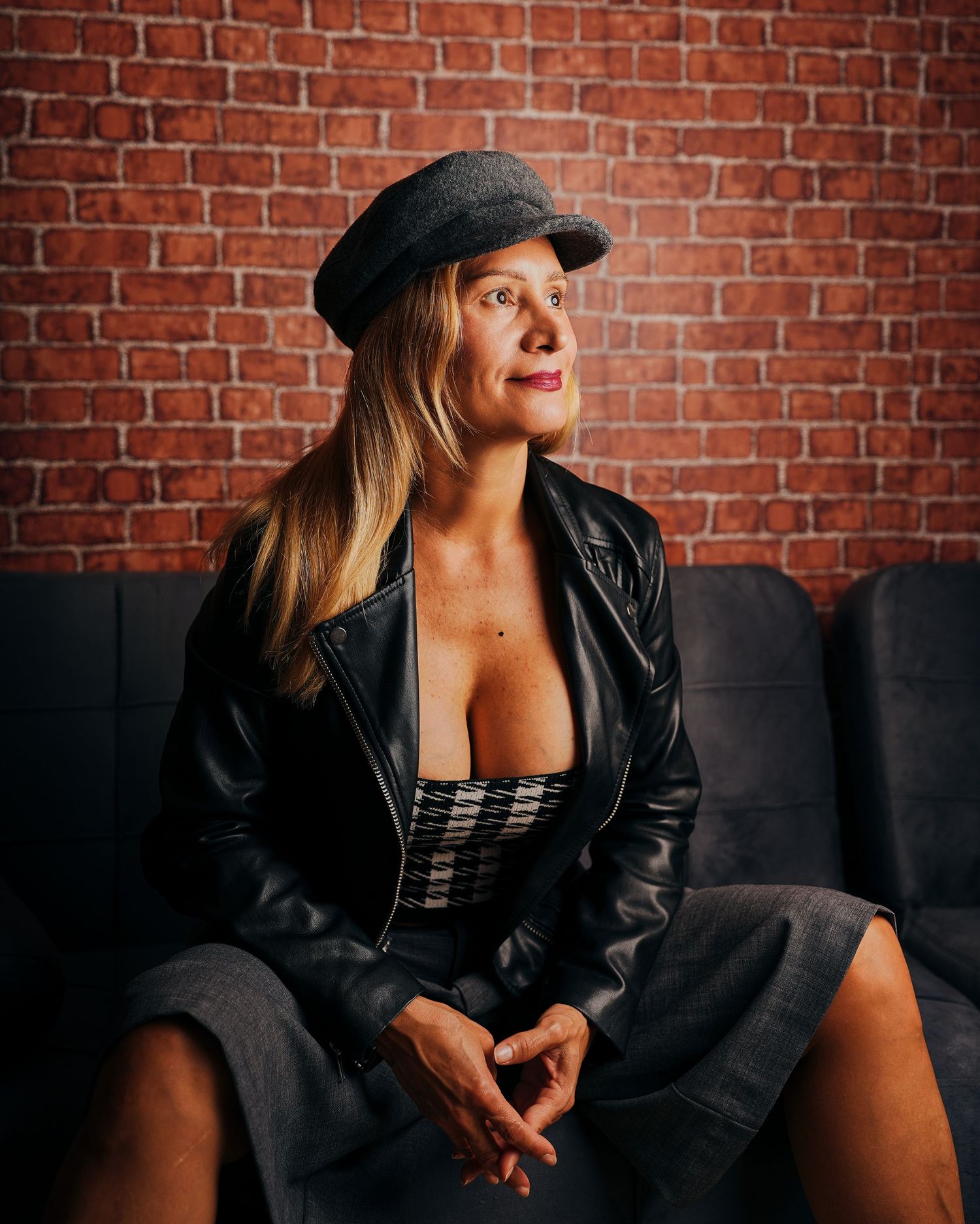 Artistic portrait against red brick featuring leather jacket and confident pose.