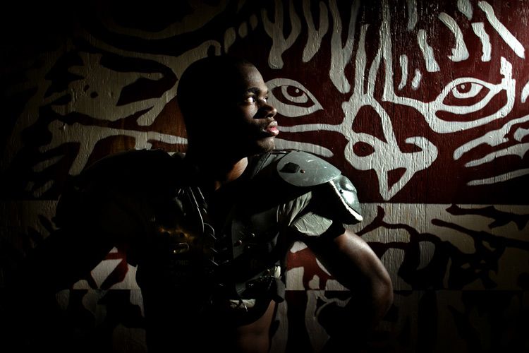 Young athlete poses confidently in front of a striking tiger mural artwork in dramatic lighting.