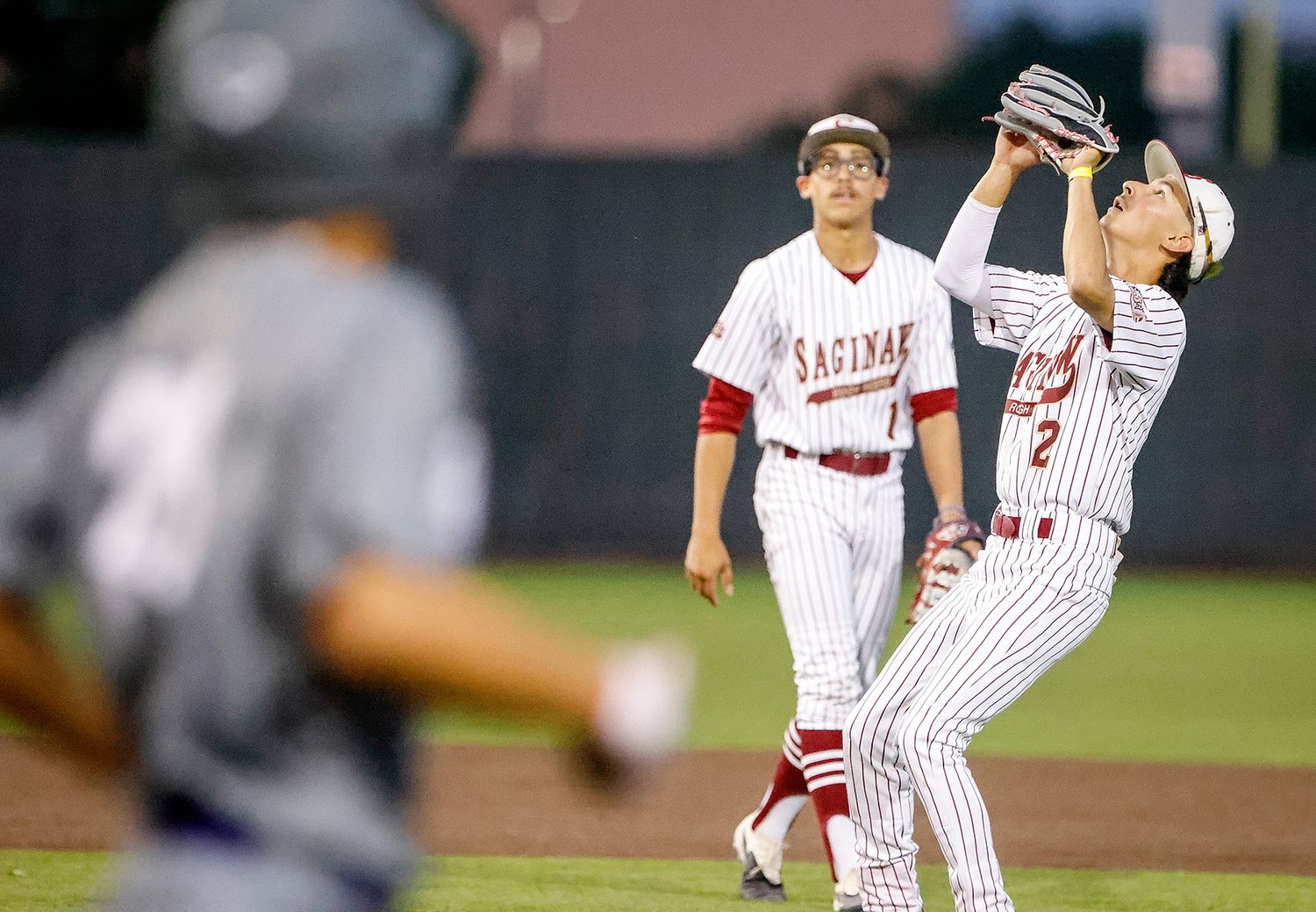 Saginaw baseball players in pinstripe uniforms during a night game, with one fielder catching a pop fly.