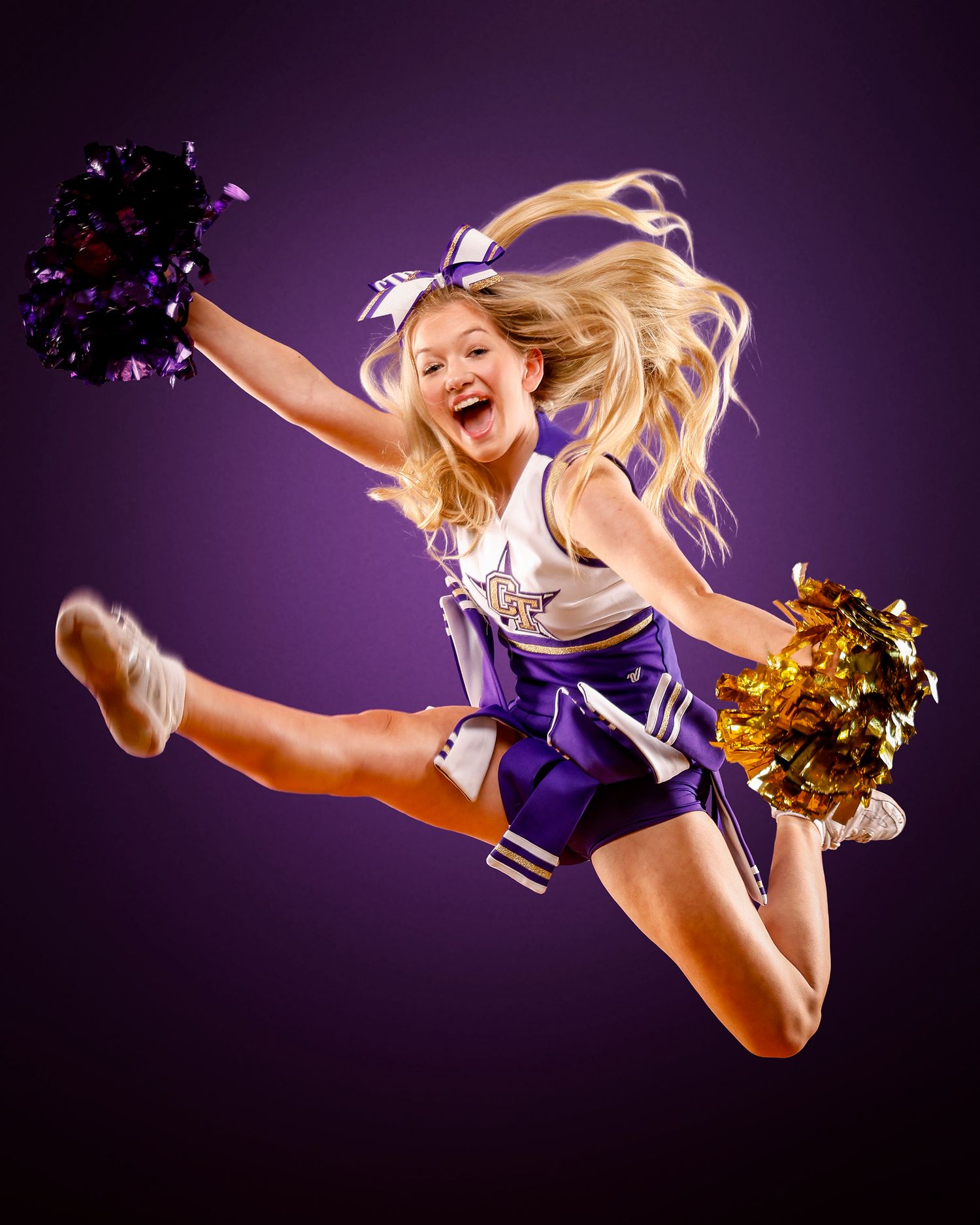 Energetic cheerleader in purple uniform leaps high with pom poms during spirited performance.