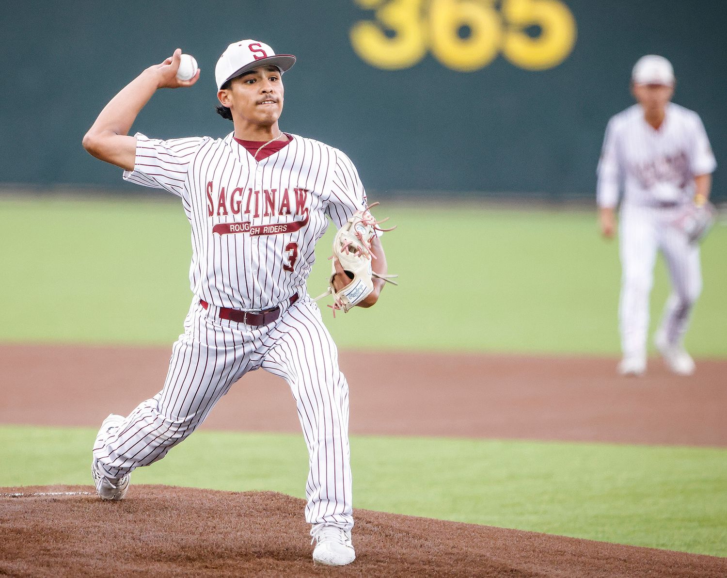 Saginaw baseball pitcher in pinstripe uniform mid-throw on the mound during a competitive game.