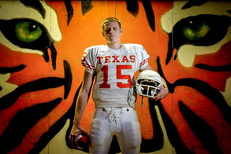 Texas football player #15 stands before a tiger mural in white uniform holding his helmet.