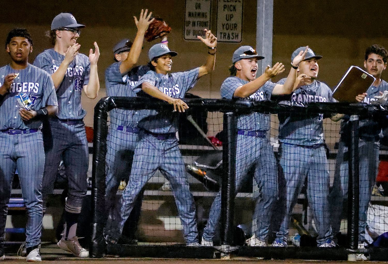 Baseball team in Rangers uniforms celebrating enthusiastically in the dugout during a night game.
