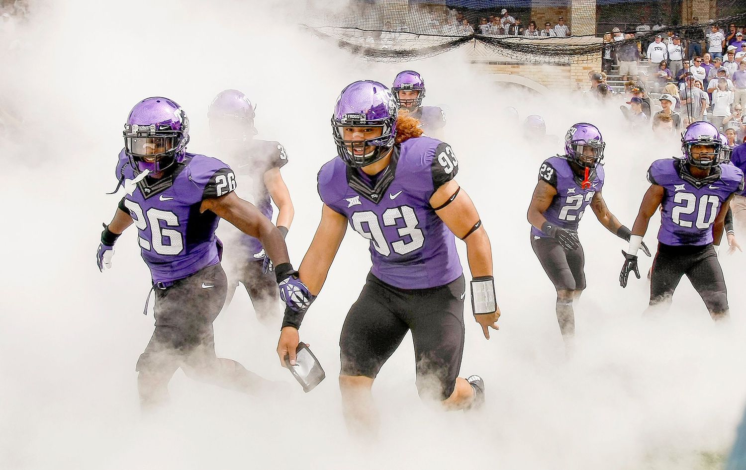 TCU Horned Frogs football players in purple uniforms emerge through smoke during a dramatic stadium entrance.