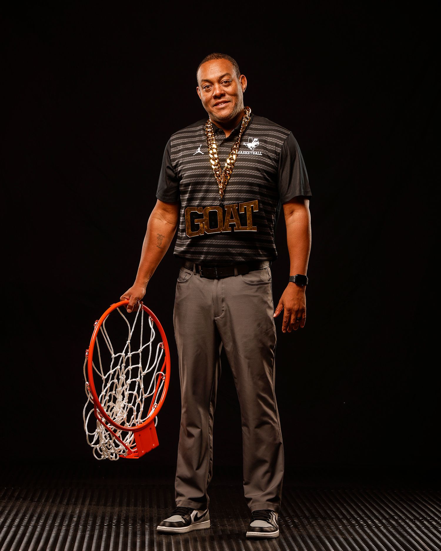 Man in GOAT chain holds basketball hoop net in studio portrait.