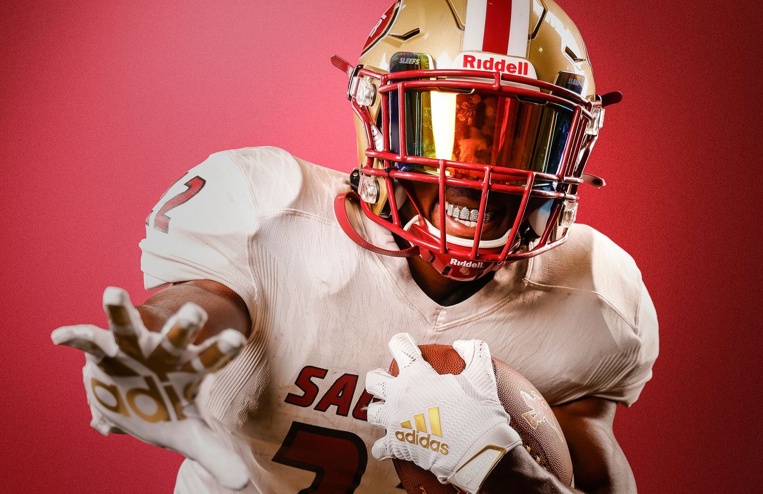 Football player in white SAC uniform with red Riddell helmet reaches forward.