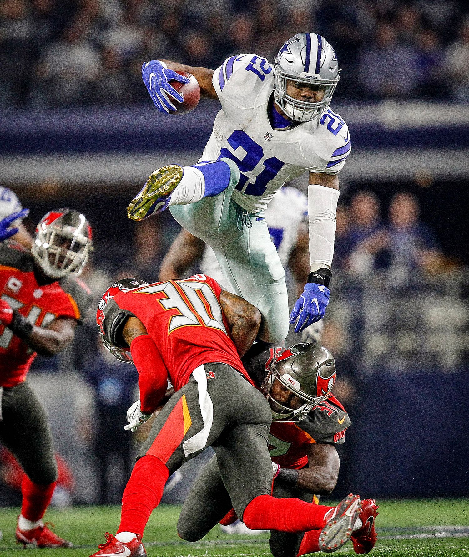 Dallas Cowboys running back #21 leaps over Tampa Bay Buccaneers defenders during an NFL game.