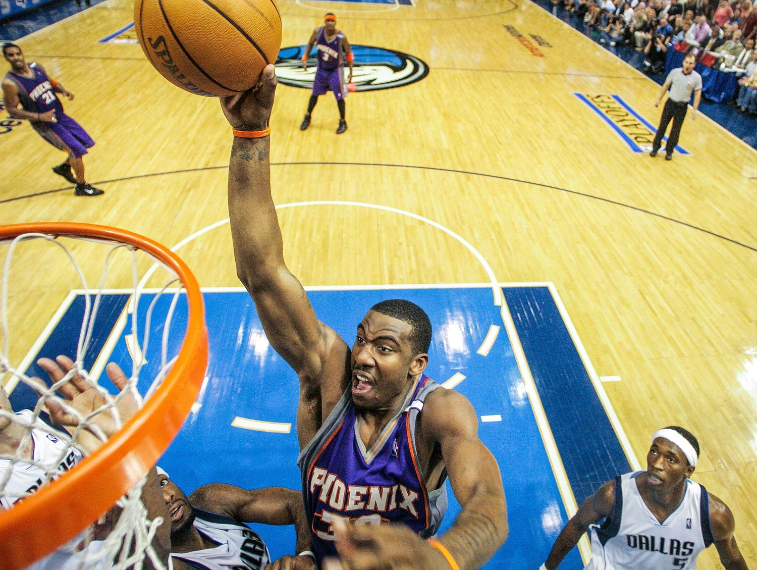 Phoenix Suns player dunks basketball over Dallas Mavericks defender.