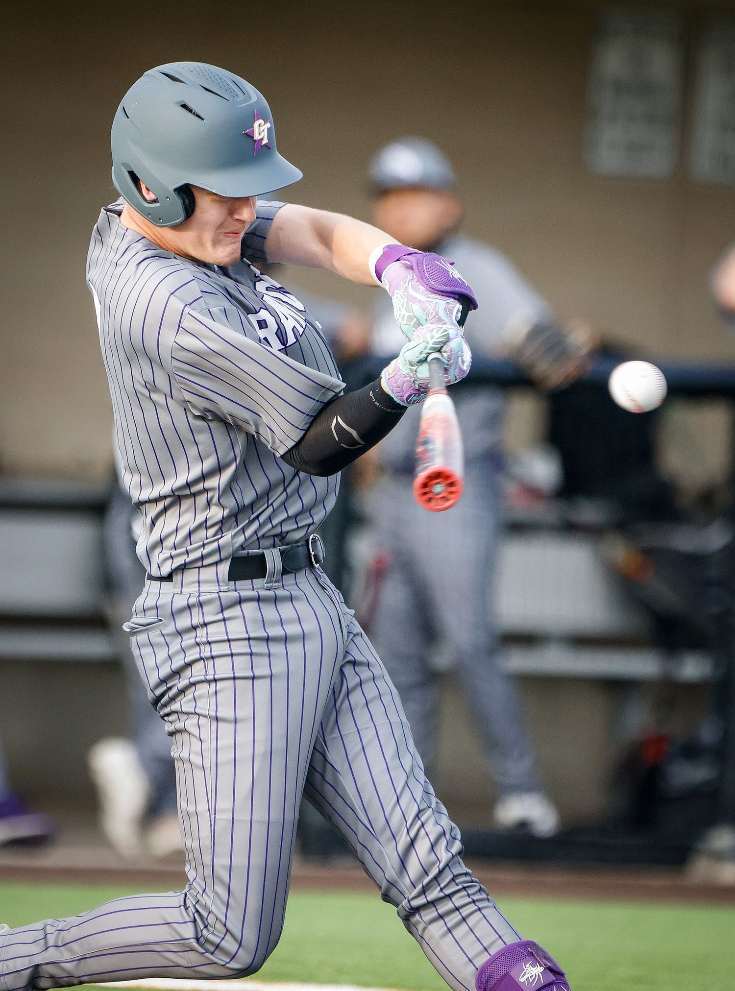 Baseball player in gray pinstripe uniform swings bat during a game, wearing purple batting gloves and gray helmet.