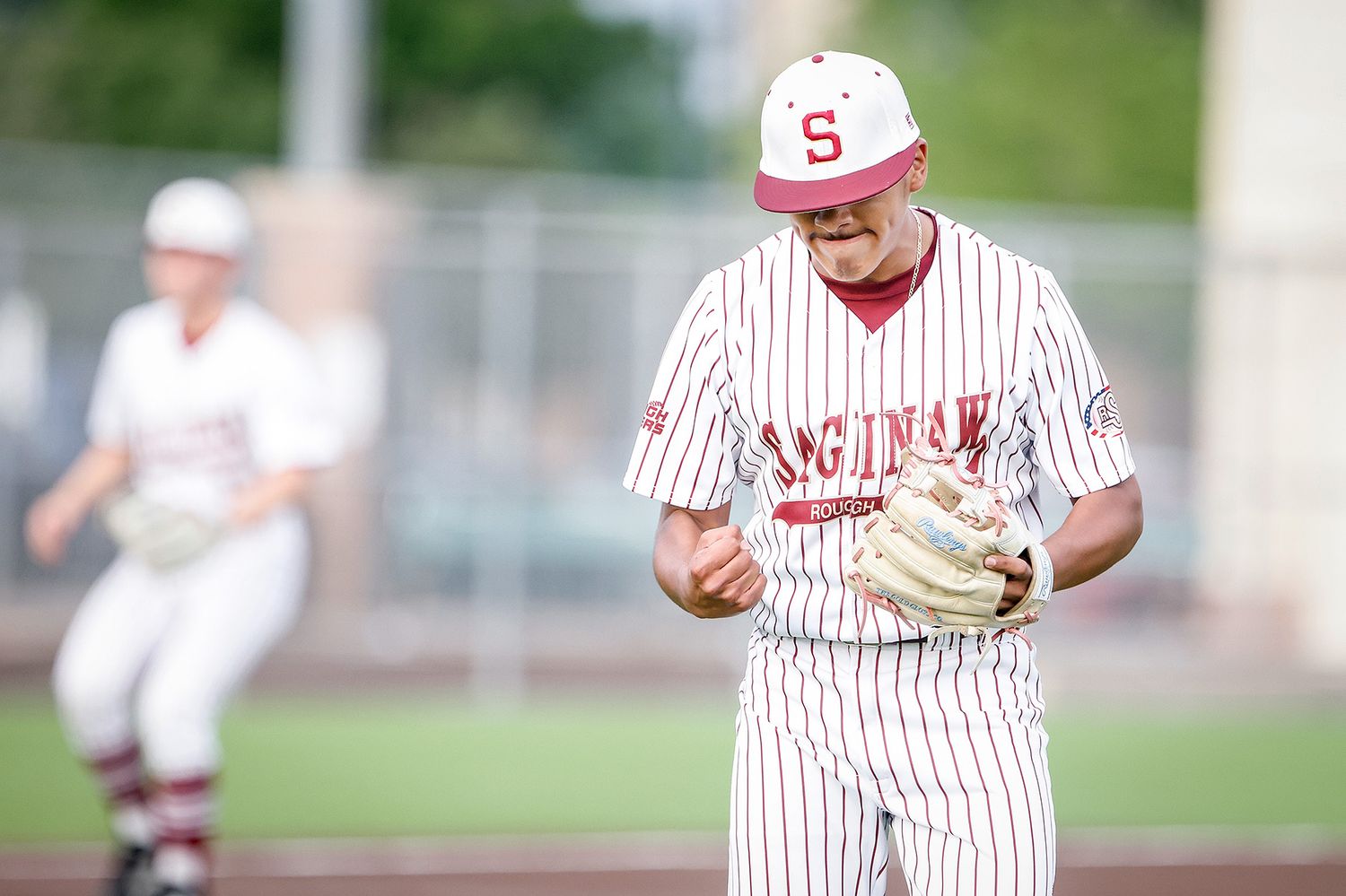 Saginaw baseball pitcher celebrates on the mound in pinstripe uniform during a competitive high school game.