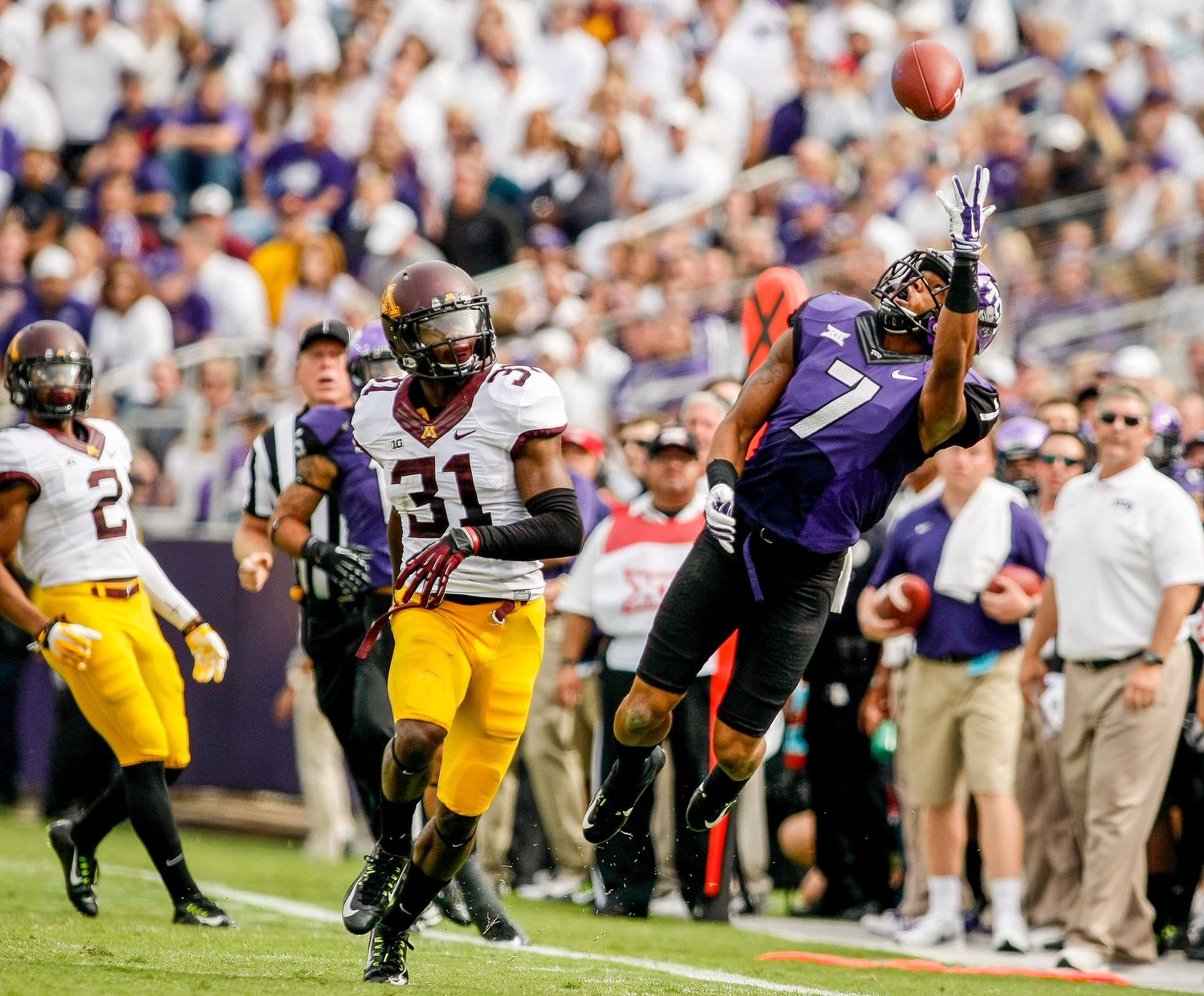 Football player #7 in purple uniform leaps to catch a pass during a college football game.
