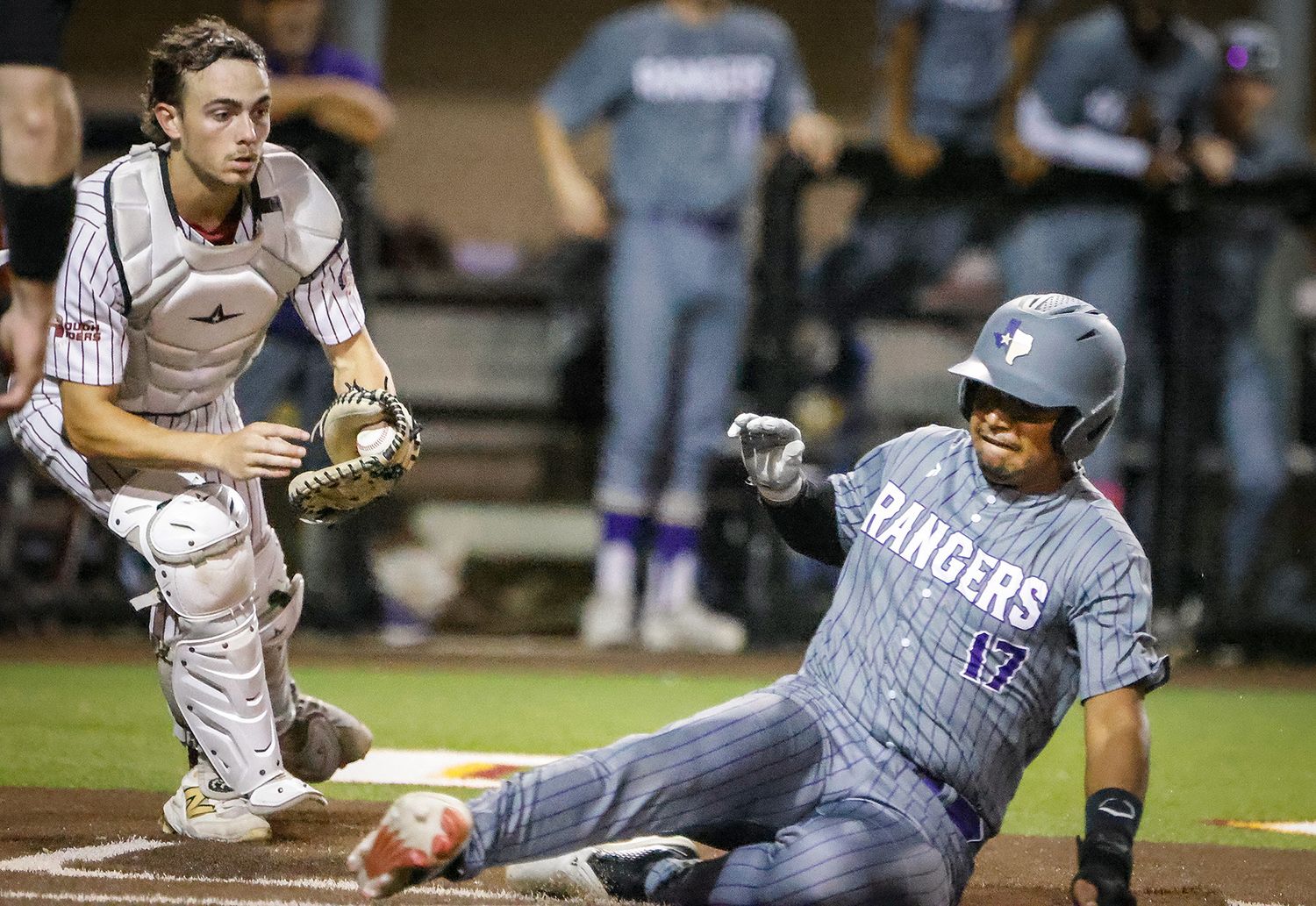 Baseball player sliding into home plate as catcher reaches to make the tag during a night game.