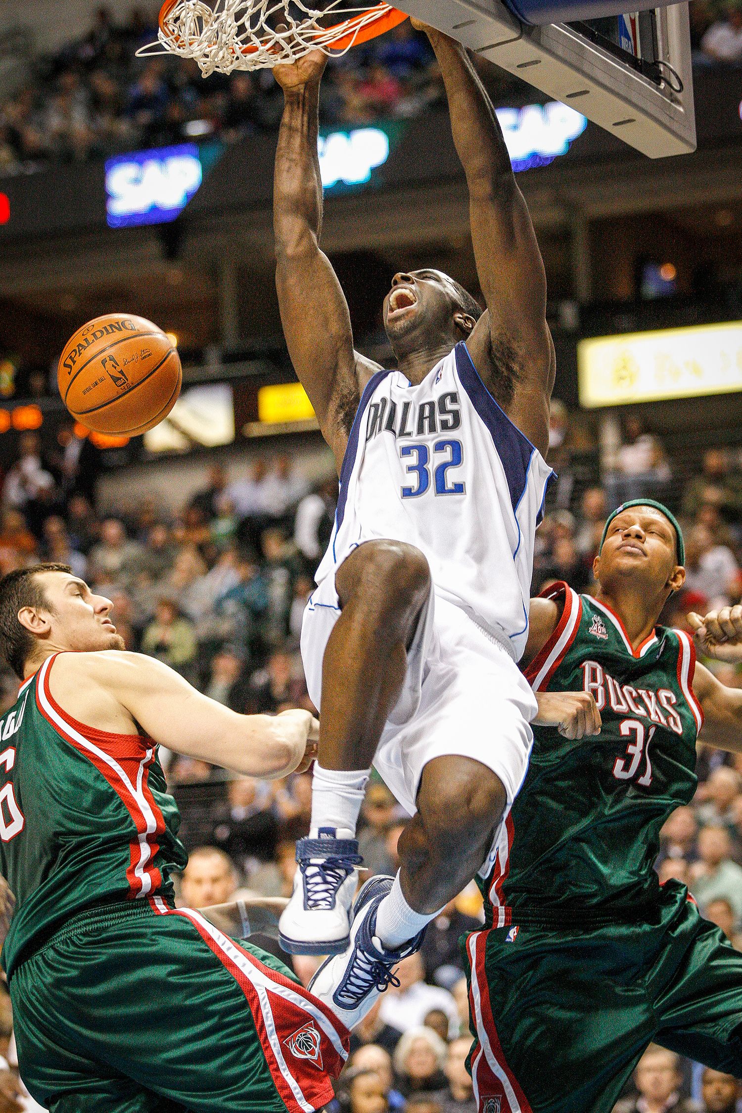 Dallas Mavericks player #32 dunks powerfully over Milwaukee Bucks defenders in an NBA game.