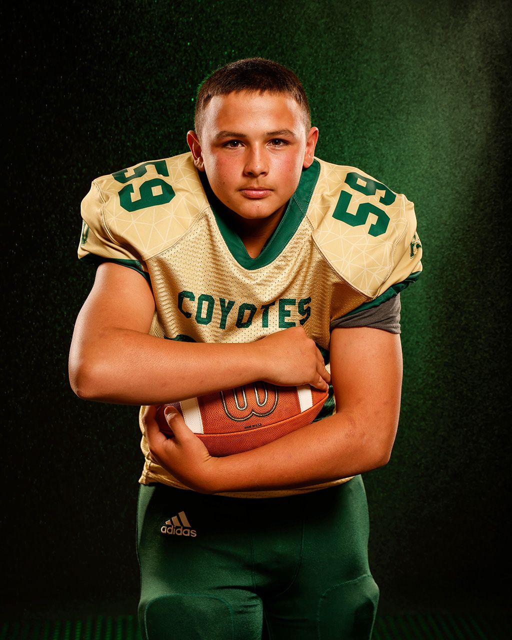 Coyotes football player #59 holds ball in gold and green uniform.