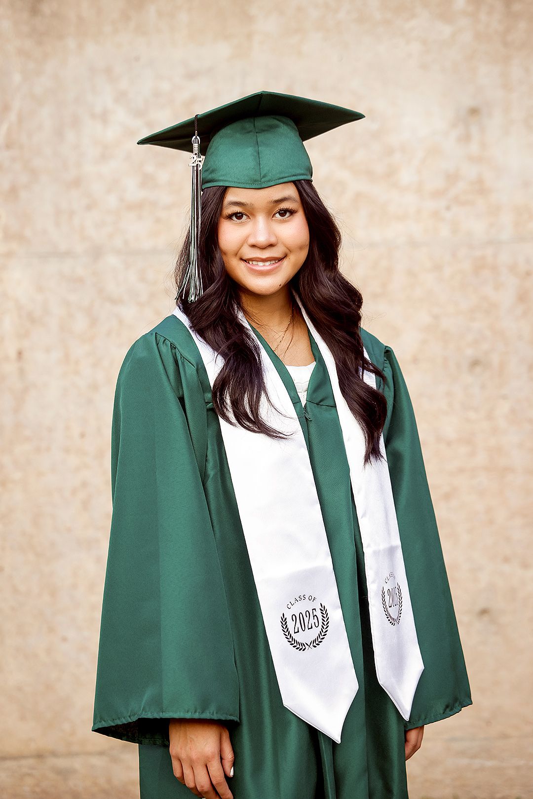 Young woman in green graduation cap and gown with class of 2005 stole, smiling for her graduation portrait.