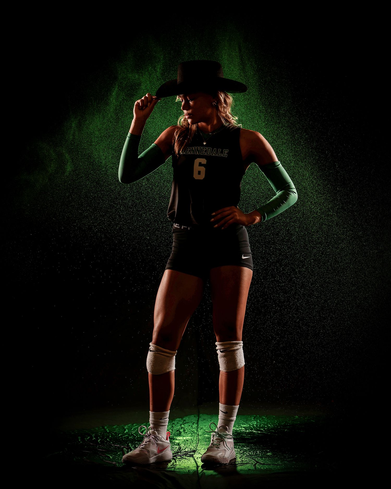 Female volleyball player number 6 poses dramatically in cowboy hat with green smoky background.