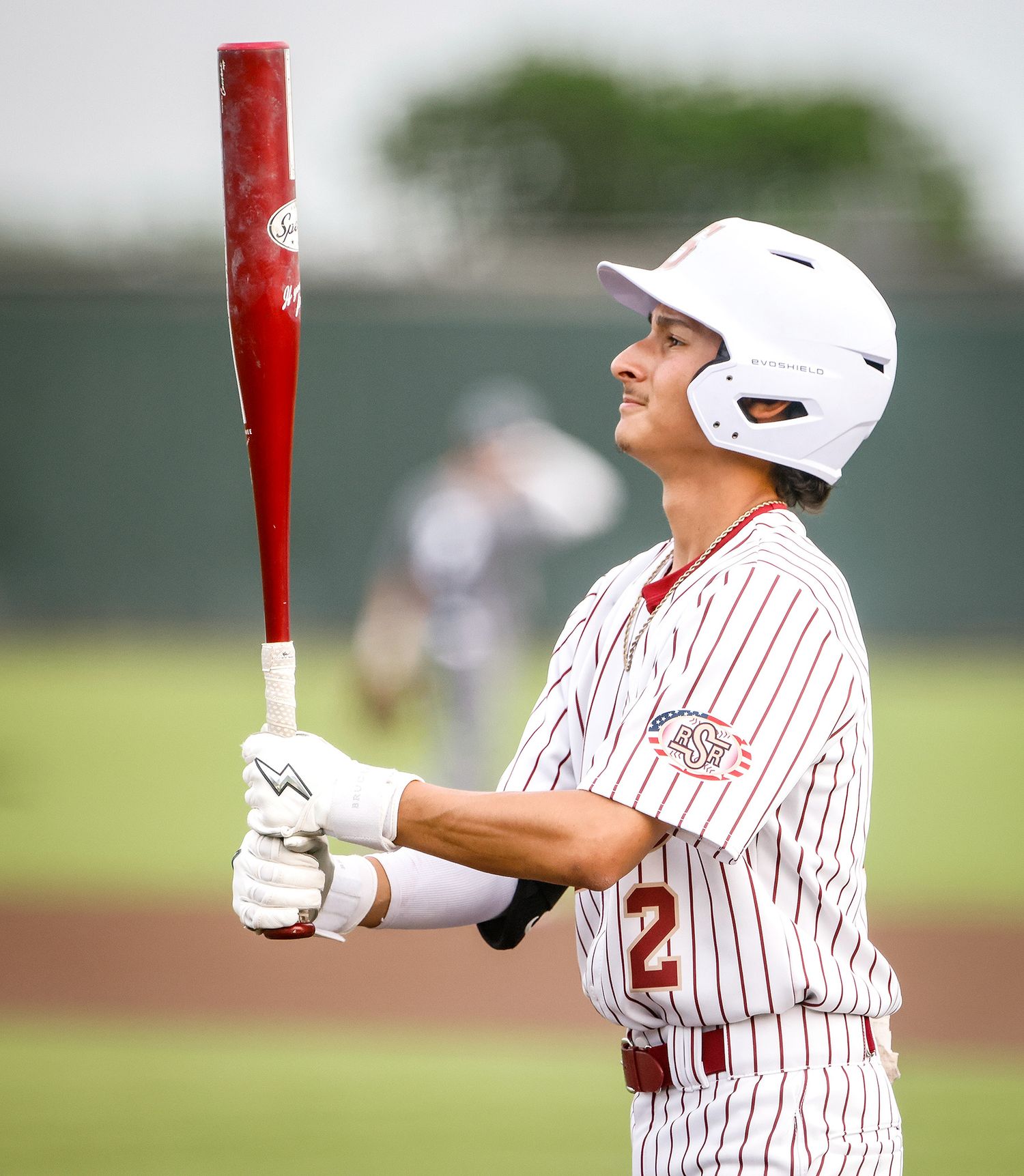 Baseball player in white pinstripe uniform holding a red bat, wearing a white helmet during a game.