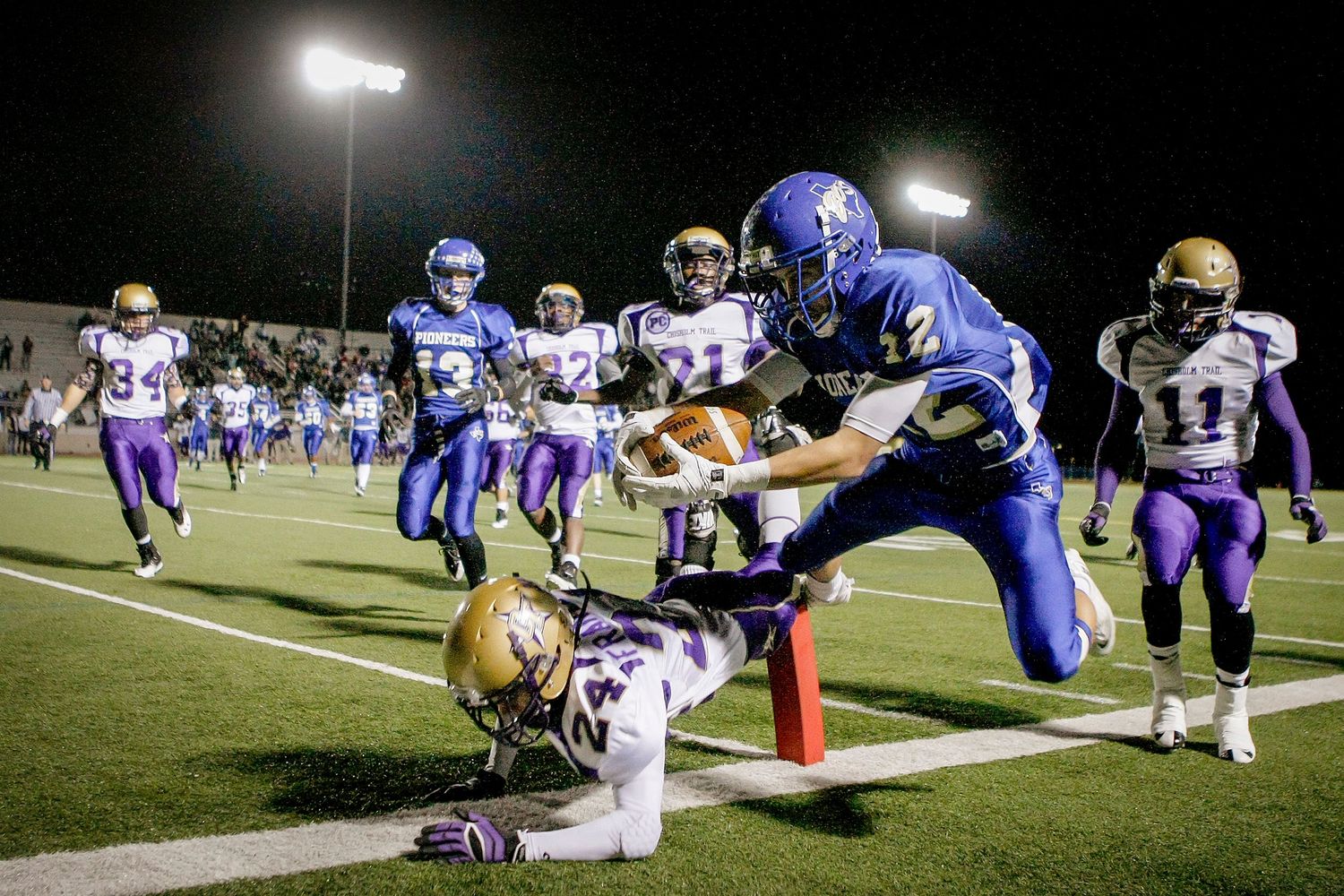 Blue team player dives for touchdown against purple team at night.