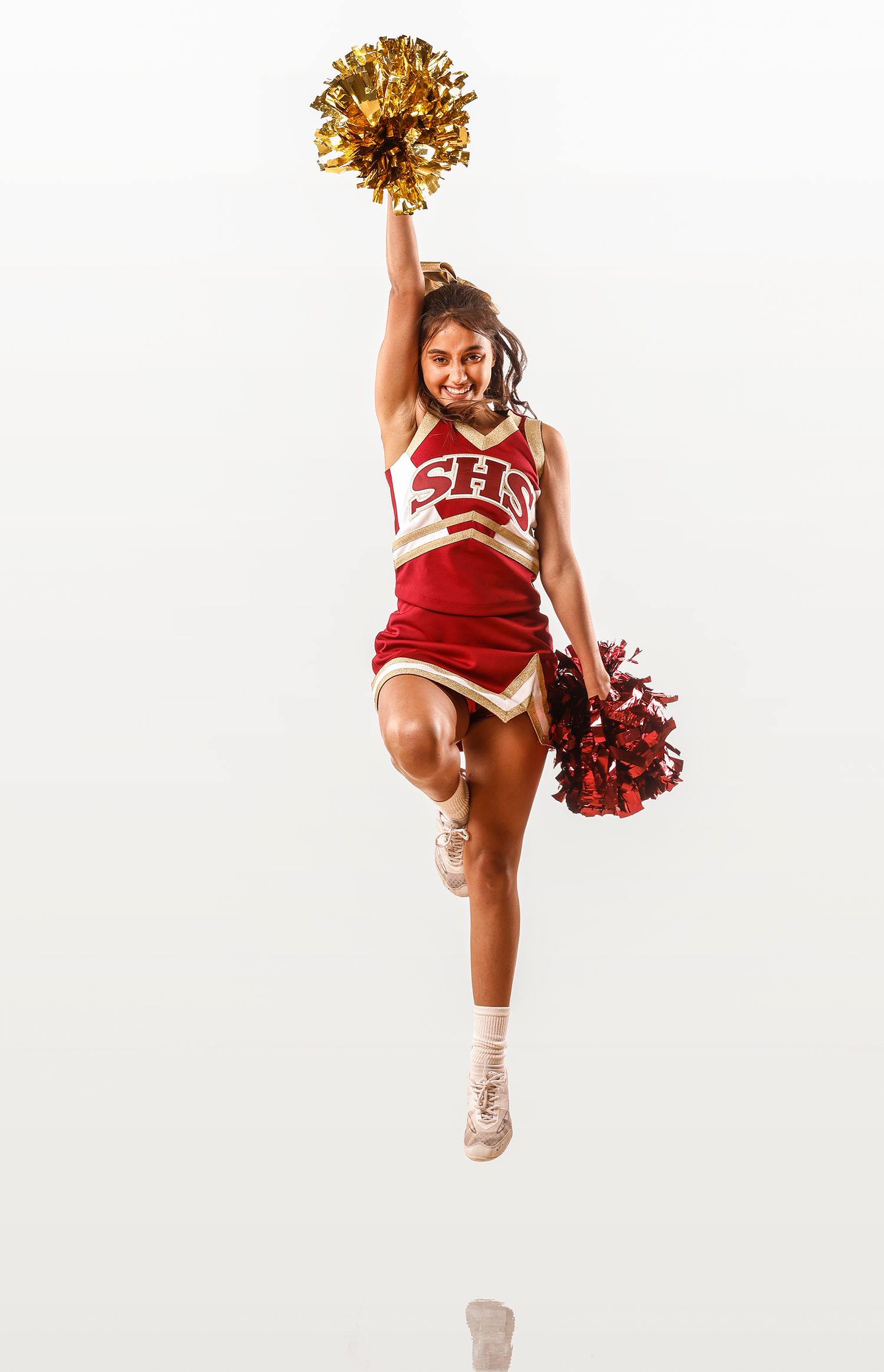 Cheerleader jumps with gold and red pom-poms in red and gold uniform.